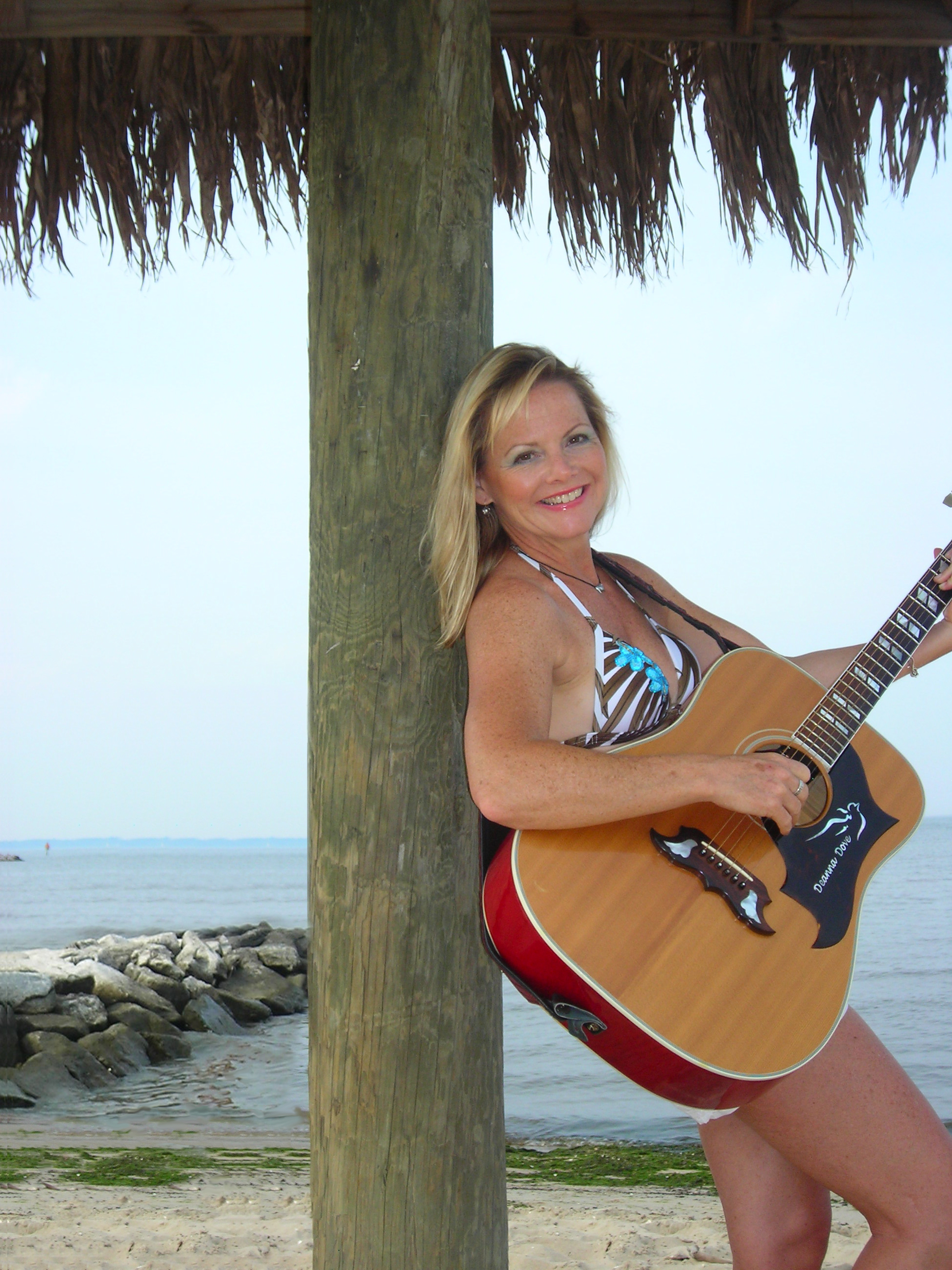 Deanna Dove performs leaning on a tropical tree with guitar