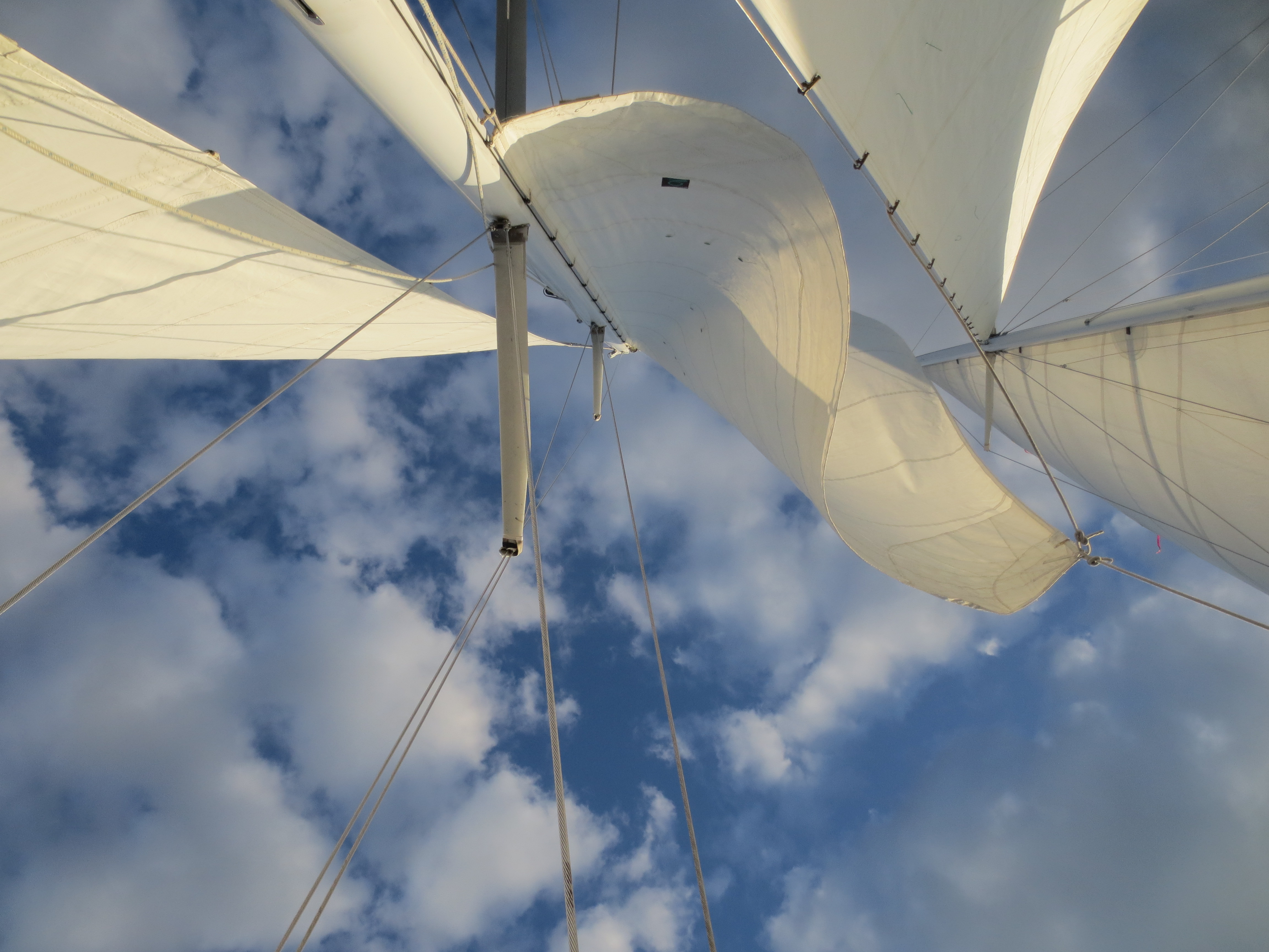 Looking up through the sails of the schooner to blue skies with white clouds