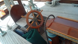 The helm.  The wheel faces aft because it is geared directly to the rudder.  You stand to one side to steer.  This is very reliable and not uncommon.