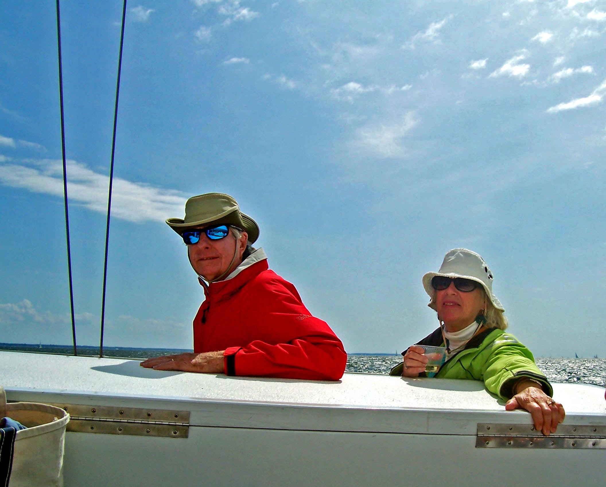 Couple one is in red jacket and one is in green jacket with beverage enjoying a sail