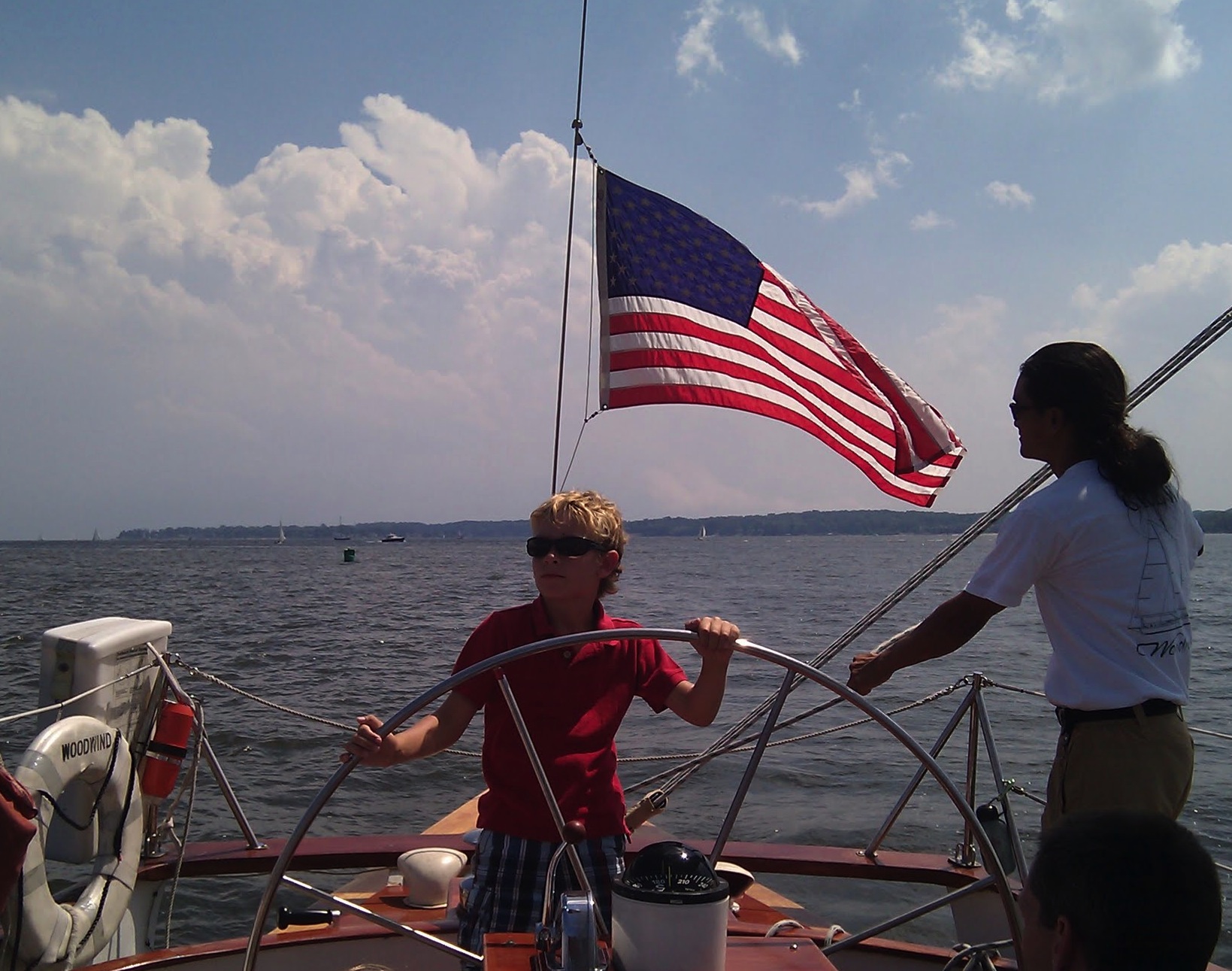 Boy steering the boat in a red shirt and blue and white shorts