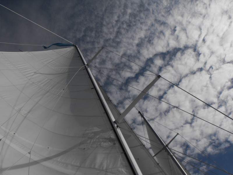 White sails going up into a blue sky with puffy clouds
