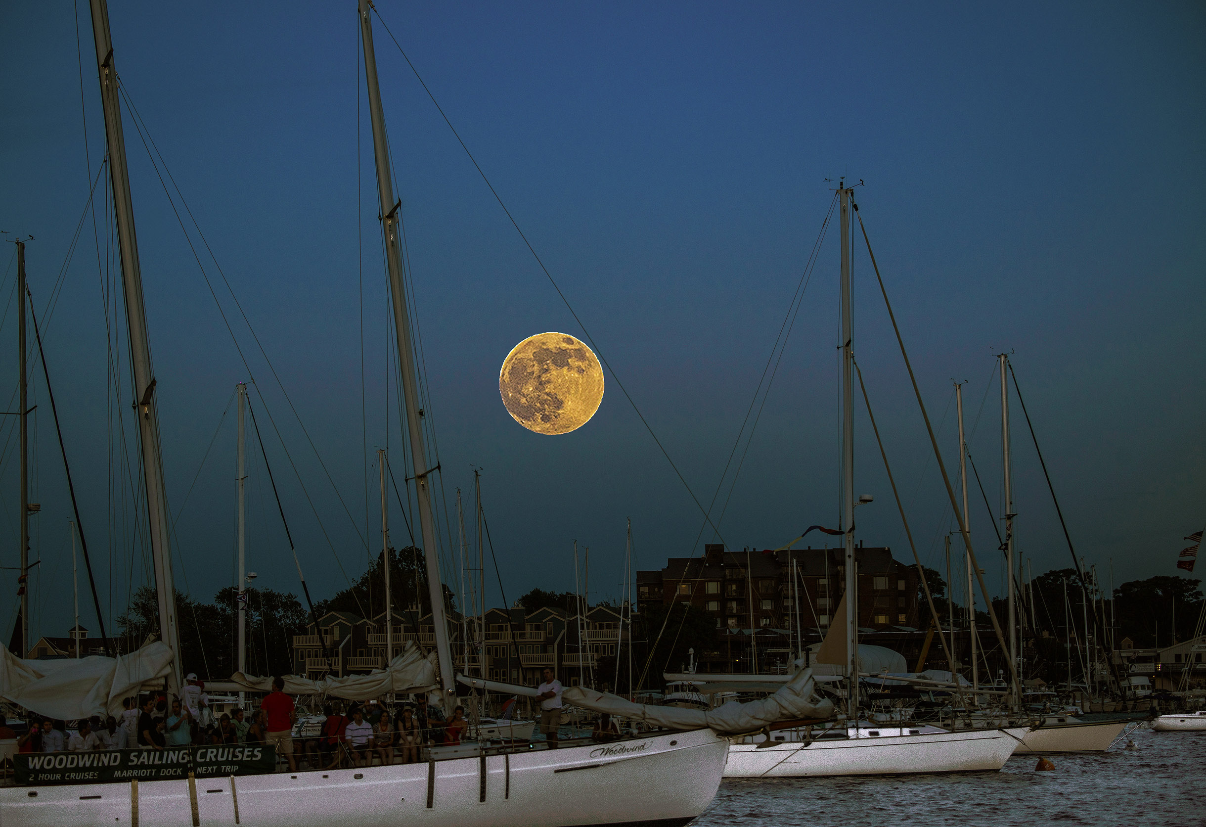 Huge ful moon over the moored sailboats in harbor