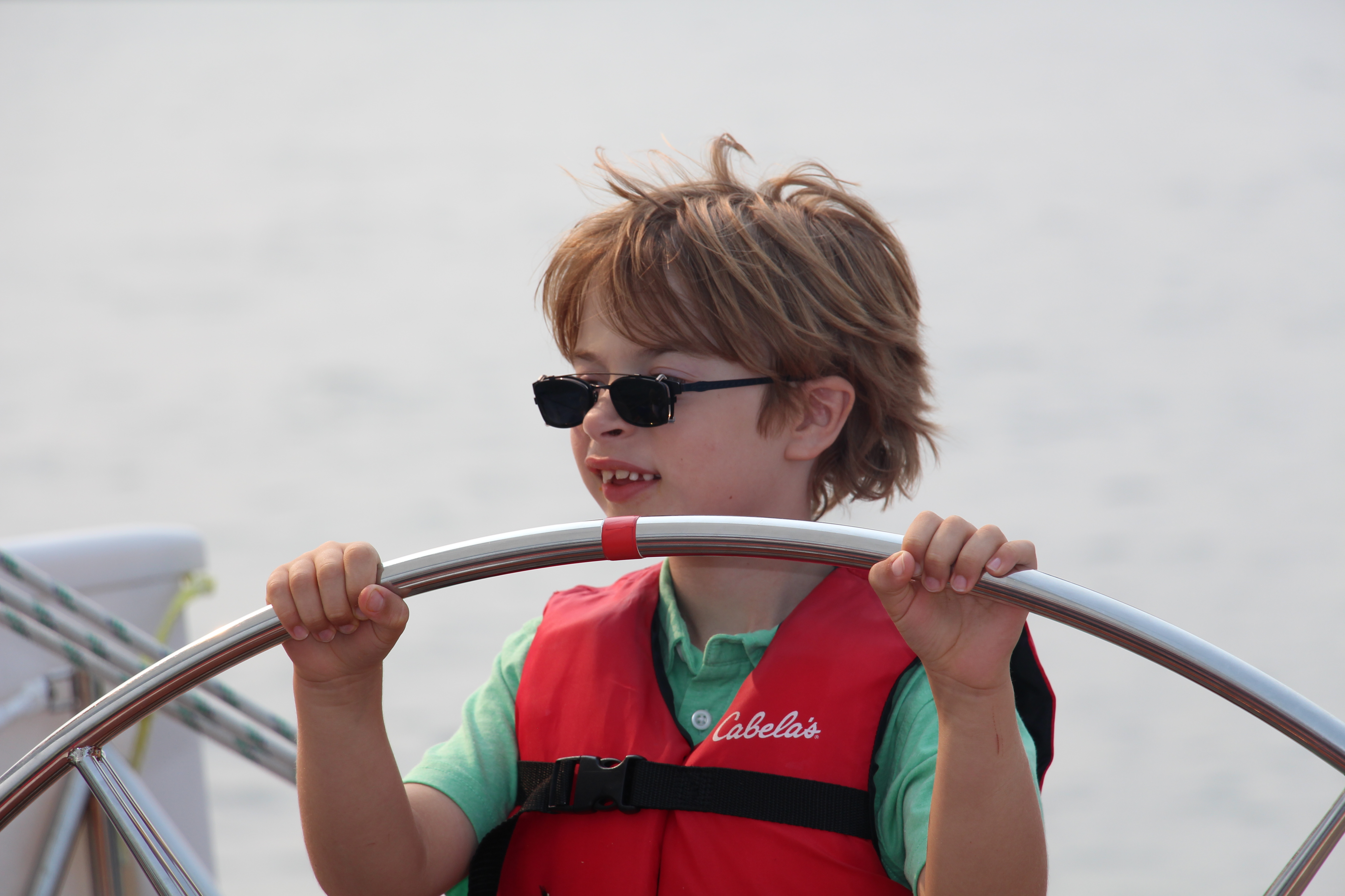Little boy with sunglasses and orange life vest steering the shcooner