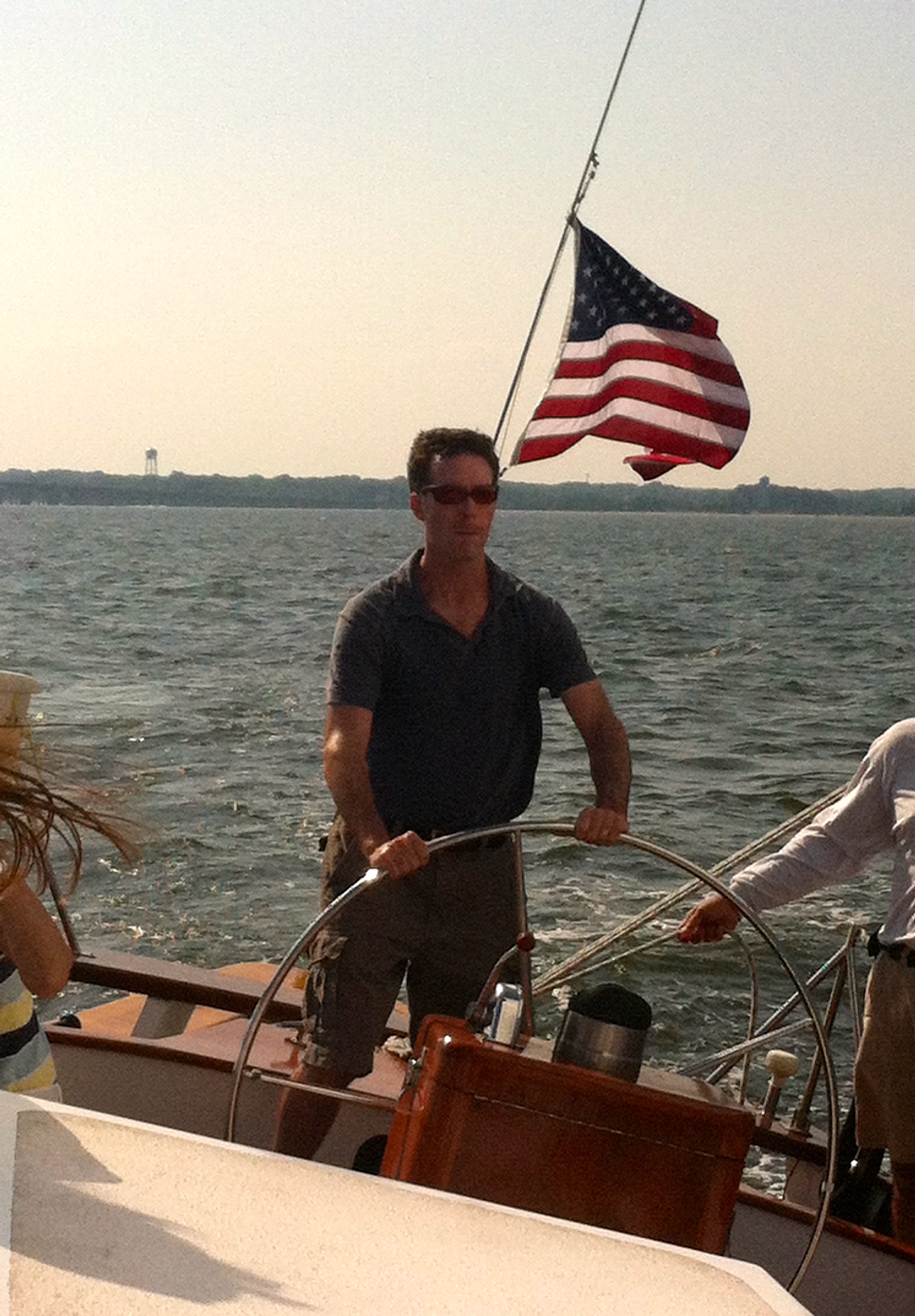 Man with American Flag behind him steering the schooner