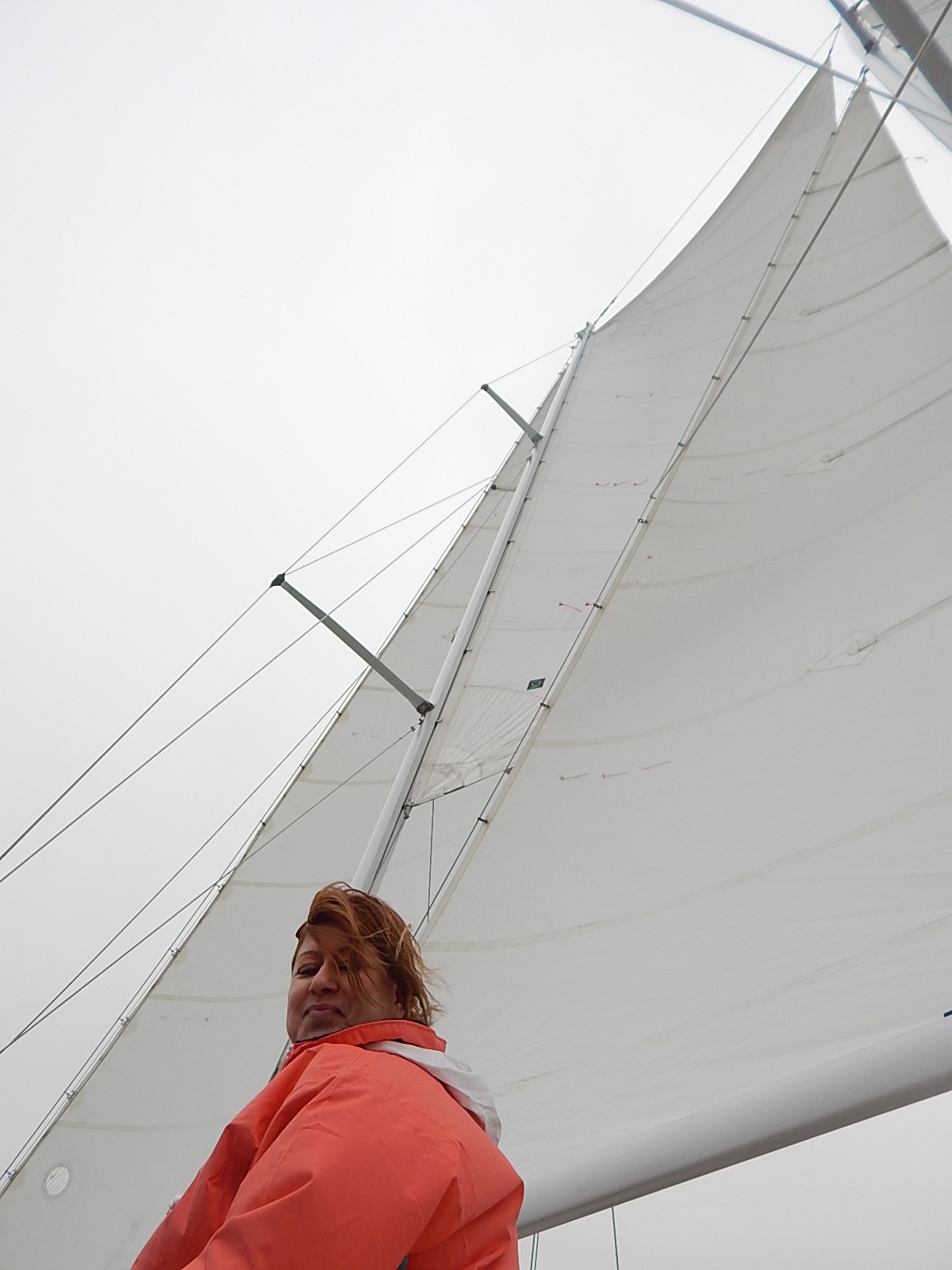 Sails full of wind and a guest in orange jacket looking at camera