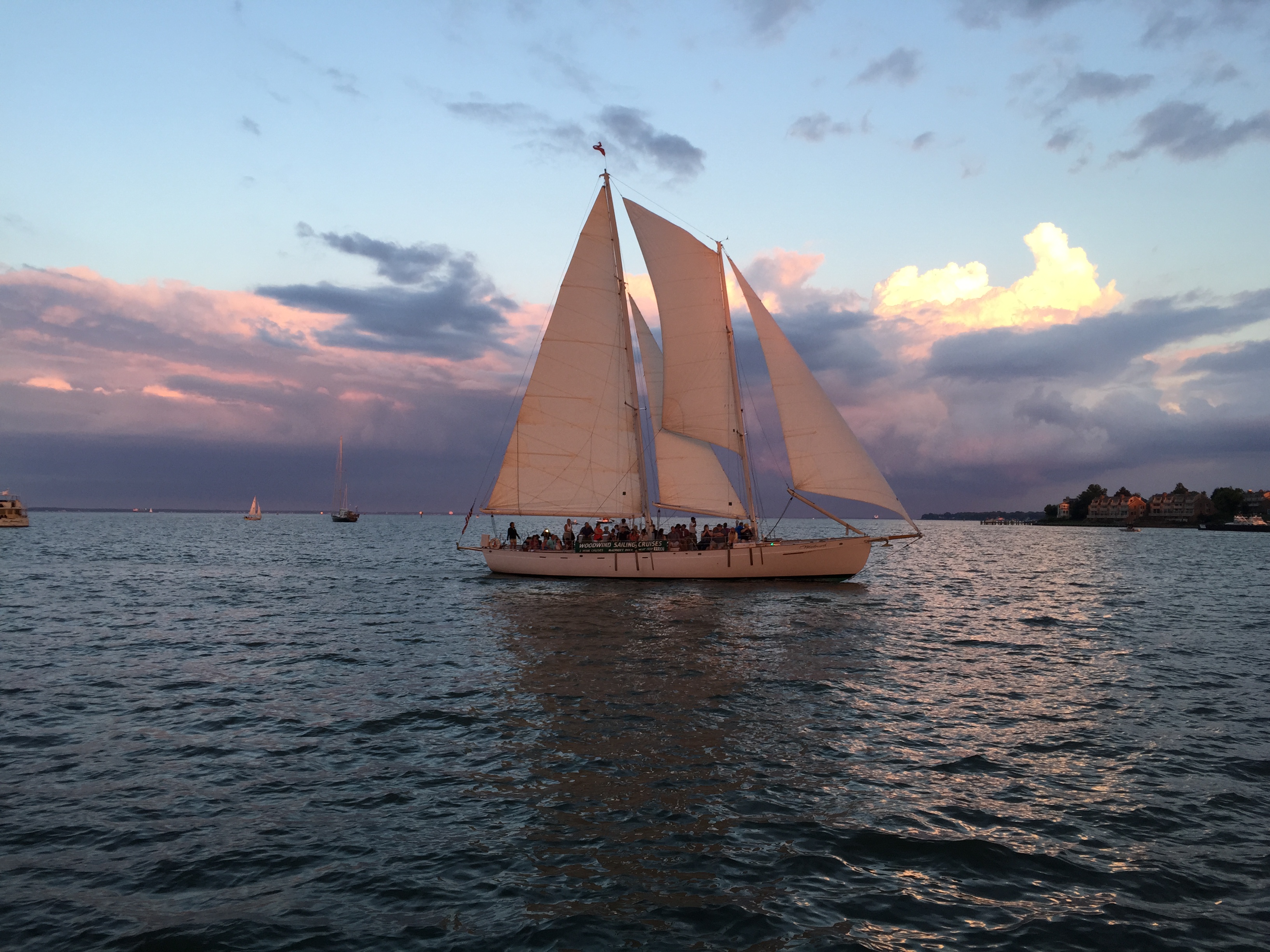 Schooner full of guests under full sunset sail on dark blue water
