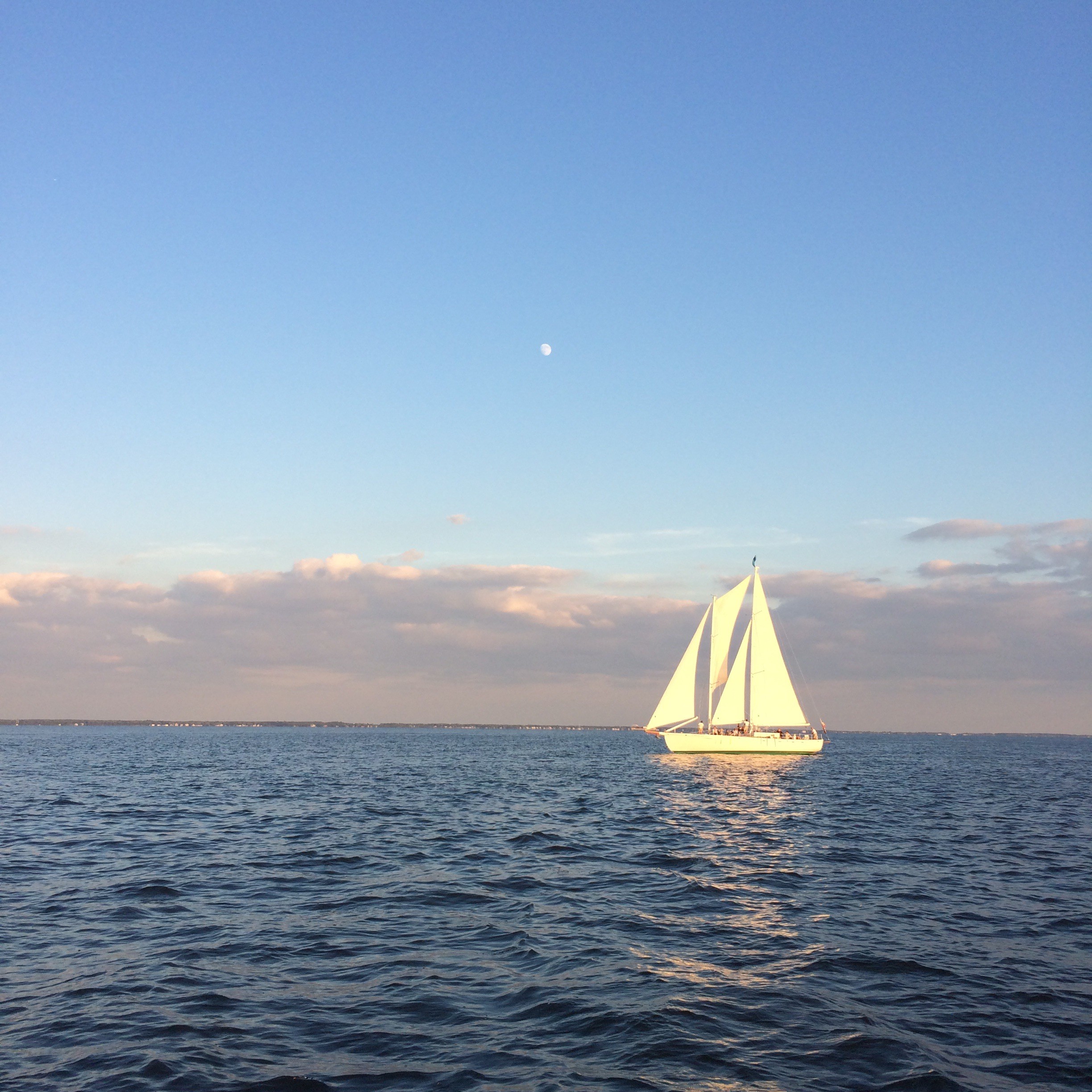 Sun reflecting off of a White Schooner on blue waters against a blue sky