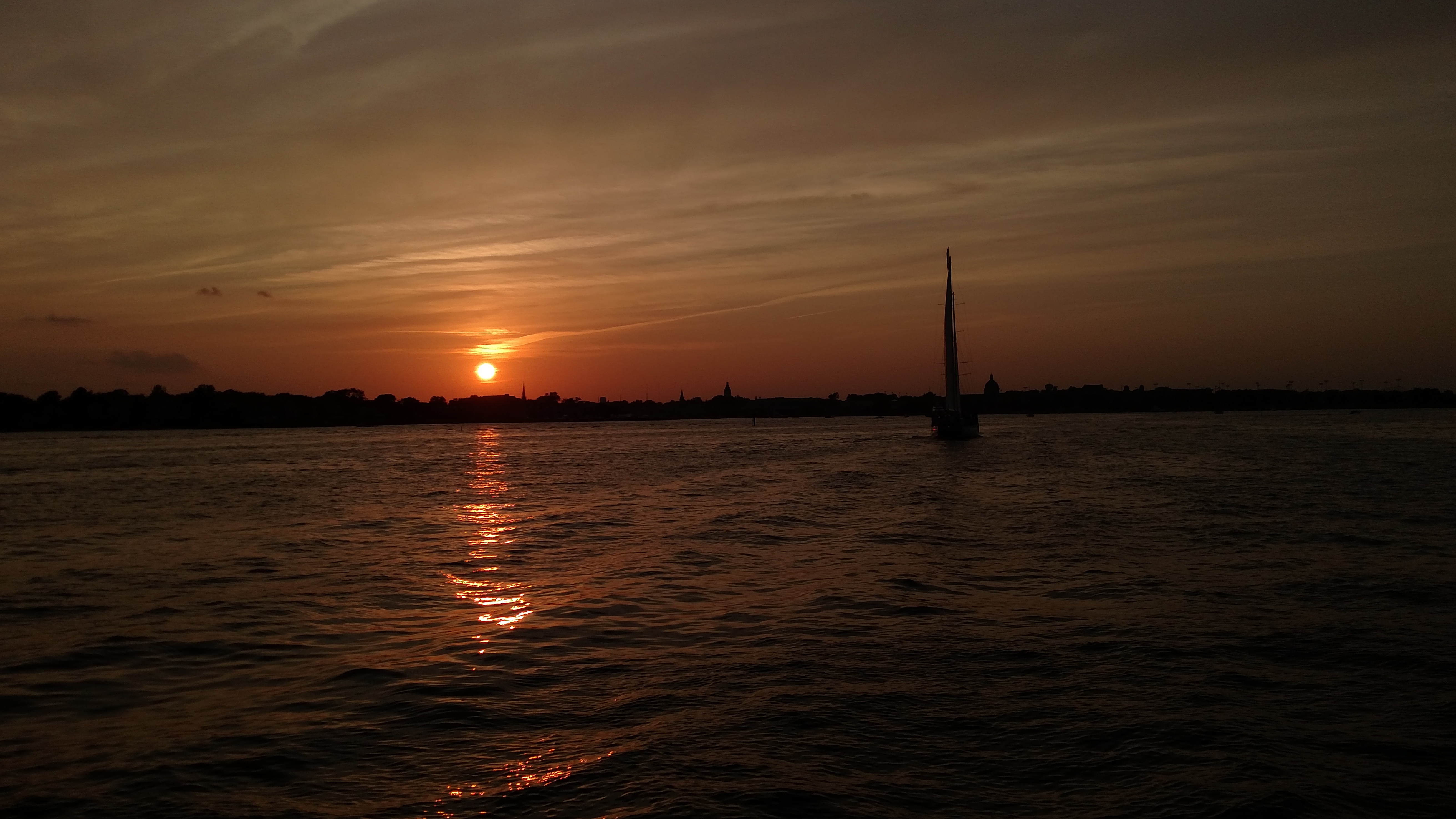 Almost dark sun setting on horizon with sailboat on water