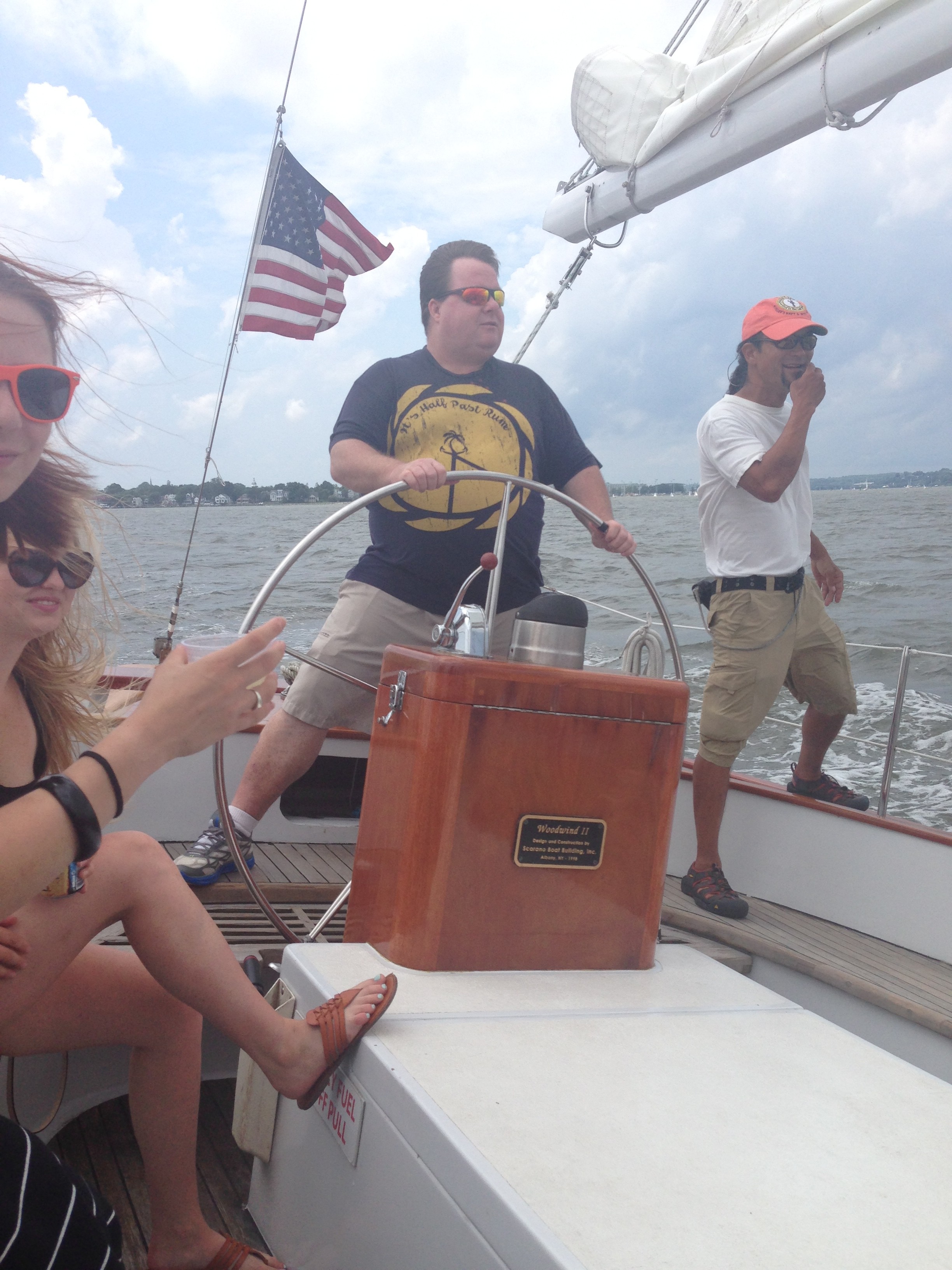 Man in gold & black t-shirt steering the schooner on a cloudy day