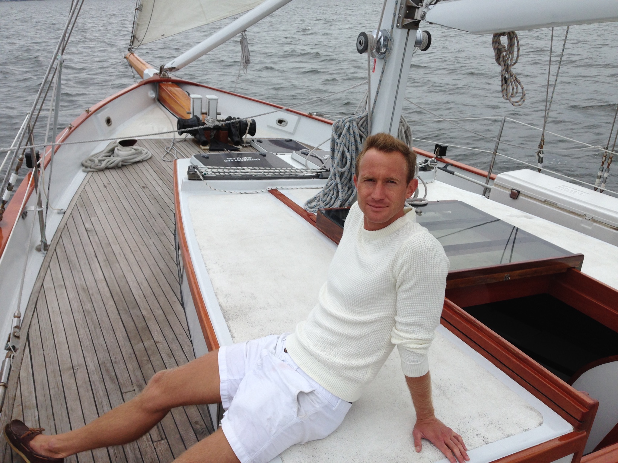 Man in white shorts and sweater leaning back and relaxing on sail