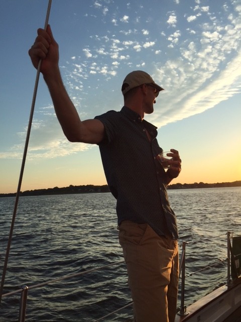 Man holding onto rigging and enjoying beverage sailing at sunset