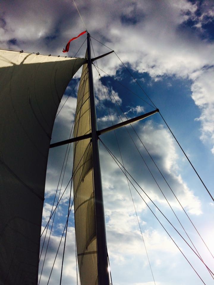 Looking up at sails on schooner into a blue sky with white clouds