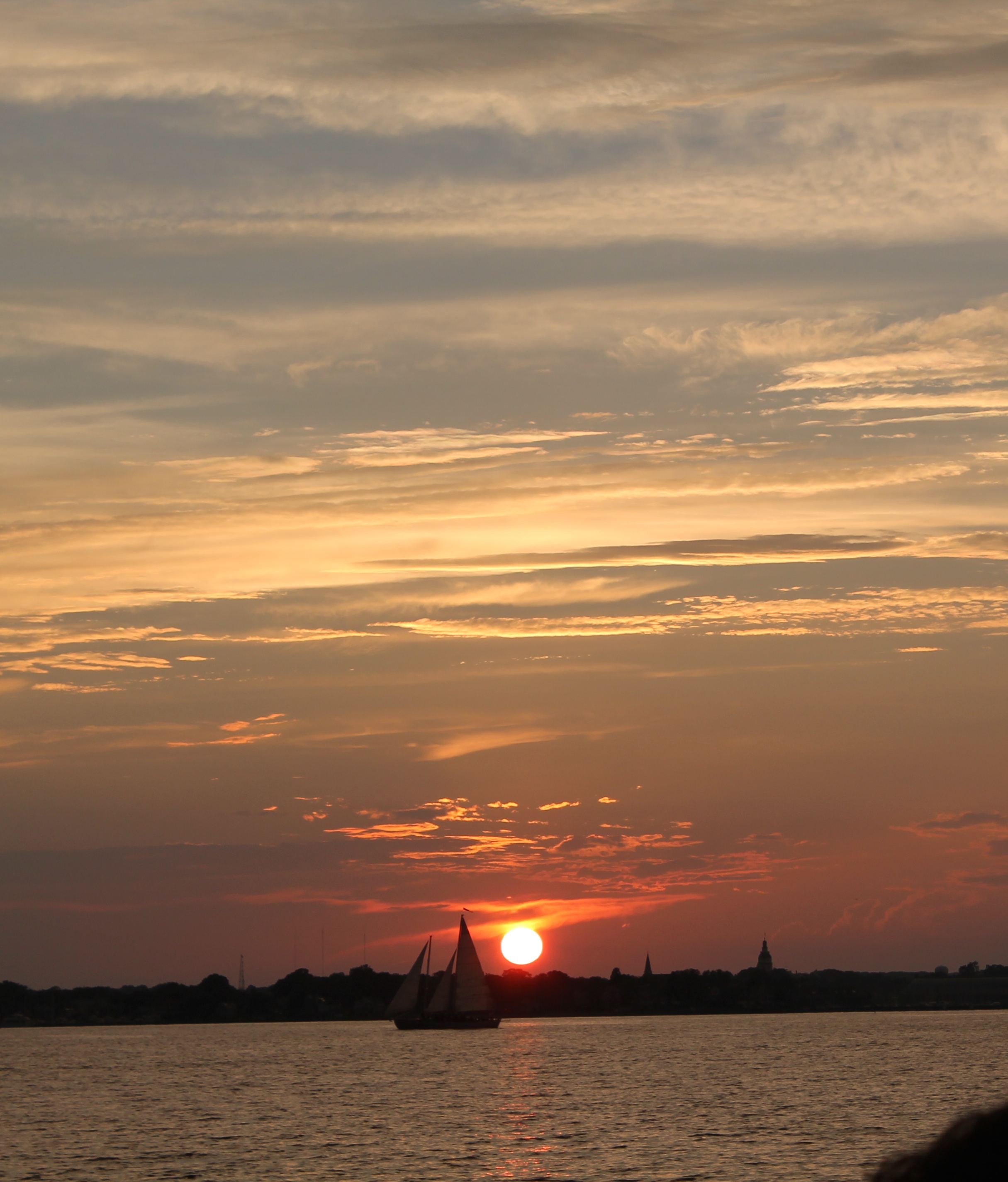 bright red ball of sun behind schooner sailing