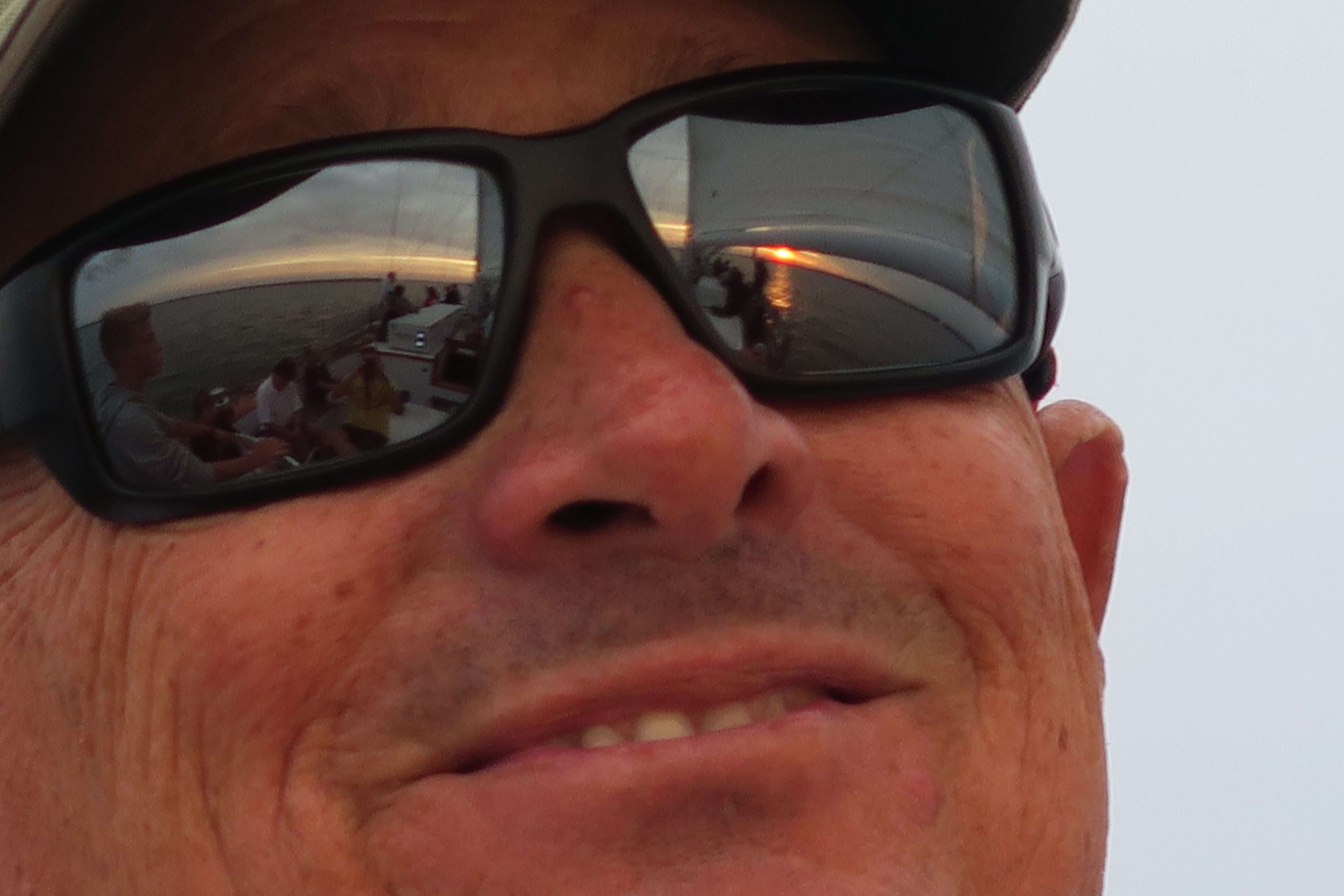 Face of man smiling with sunset reflected in his glasses