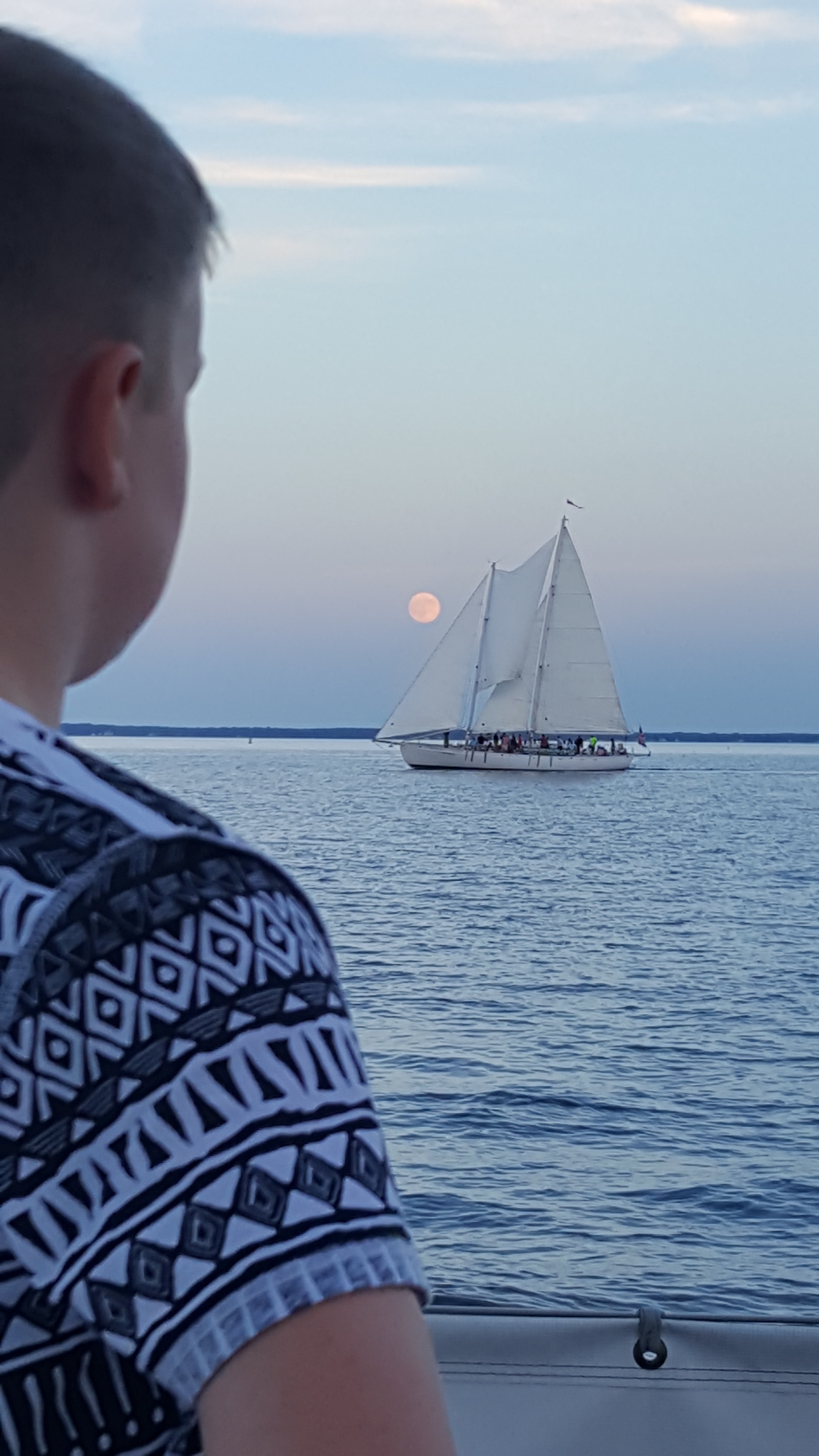 Man looking out over water at Schooner with Moon rising above it