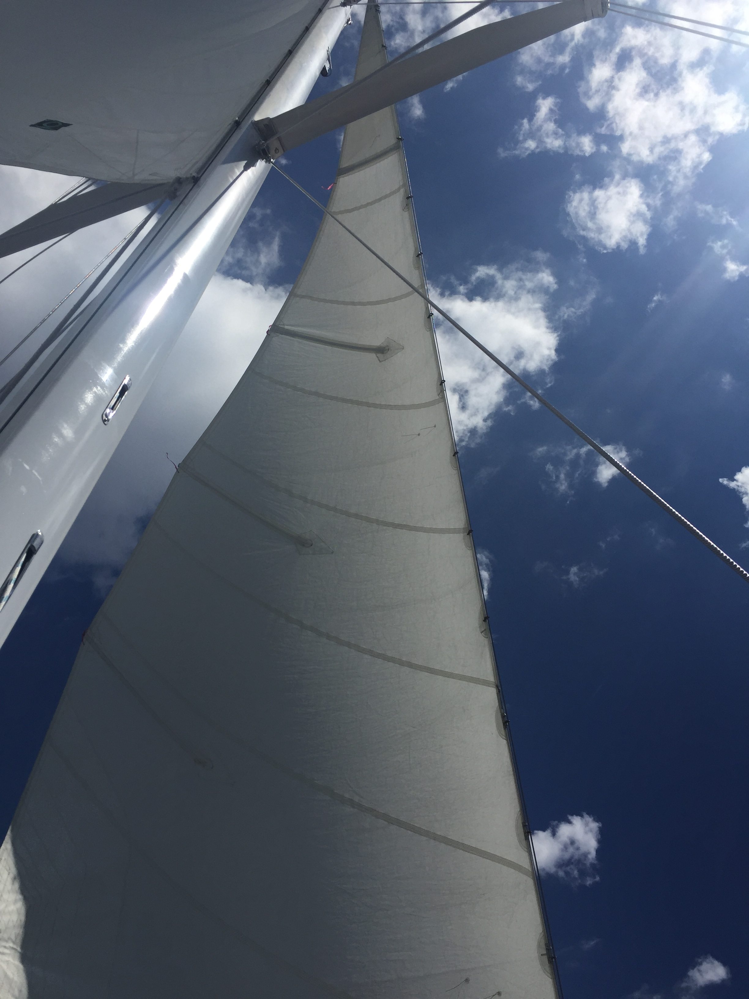 Full white sail and mast in looking up into blue sky with white clouds
