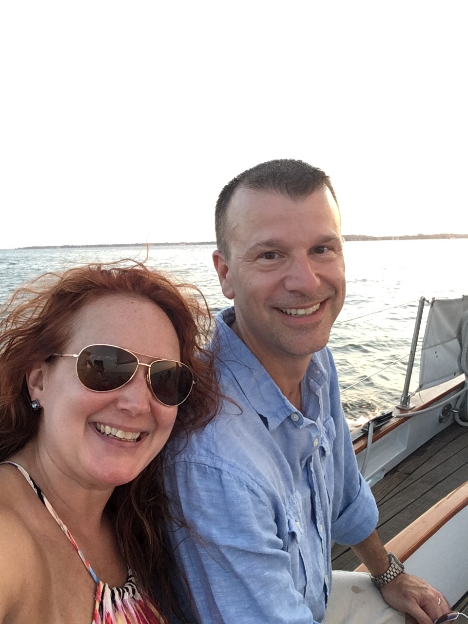Smiling couple sitting on the deck of schooner with water behind them