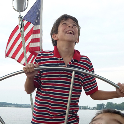 Young boy looking up at the sails in a striped shirt while steering the boat