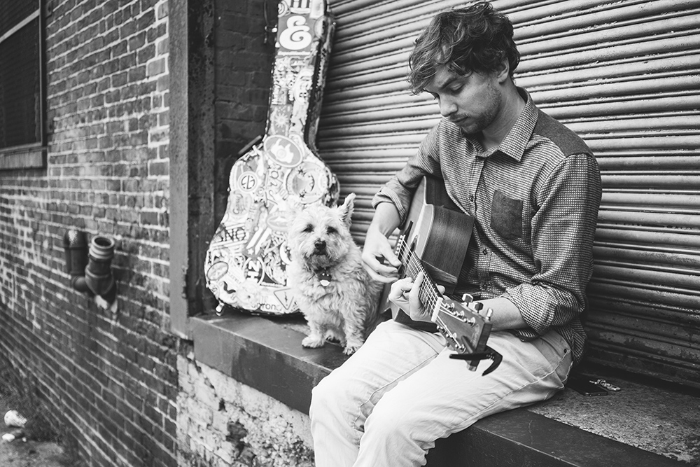 Chris Diller playing guitar with little dog sitting with him