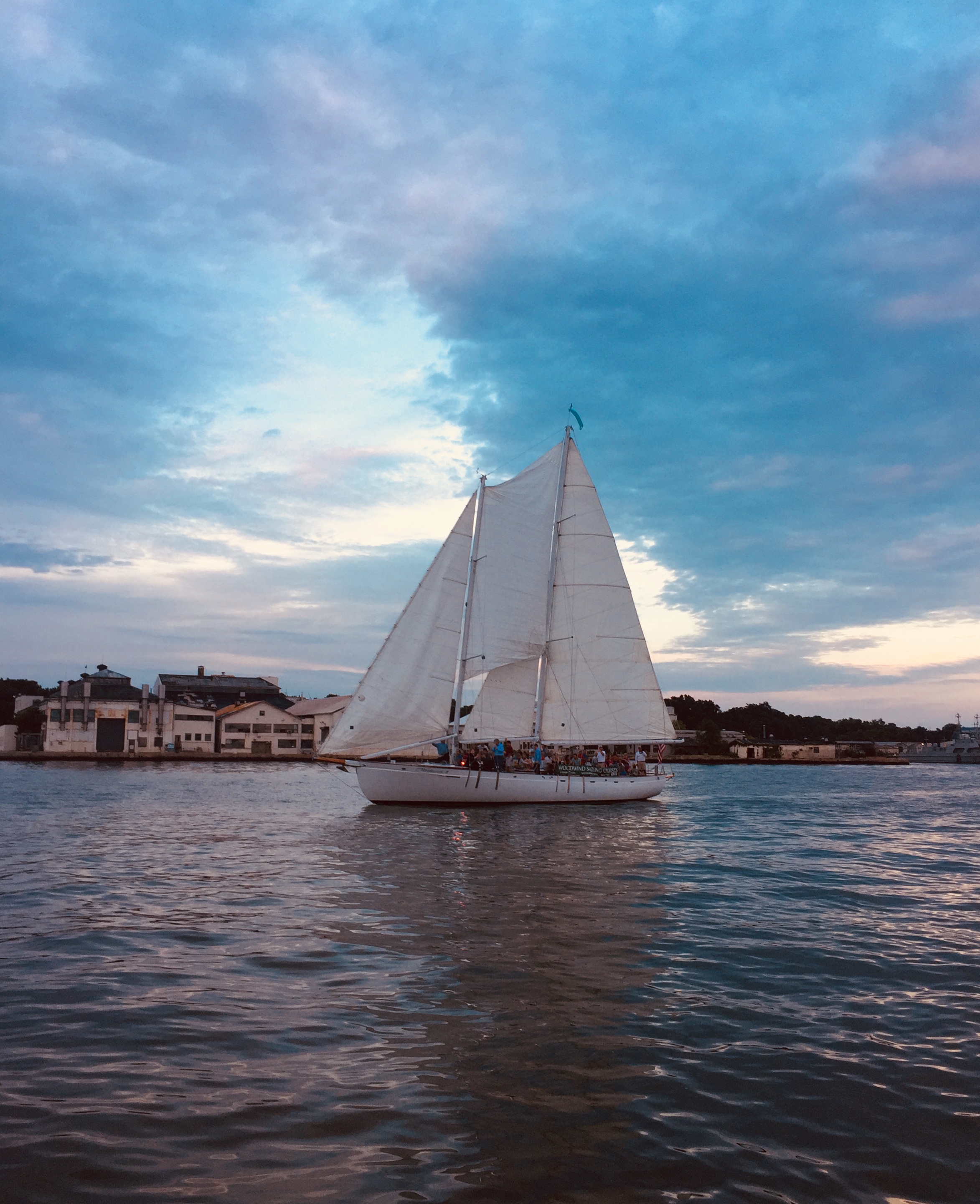 Schooner sailing in dark blue waters reflecting pinks and blues from sky