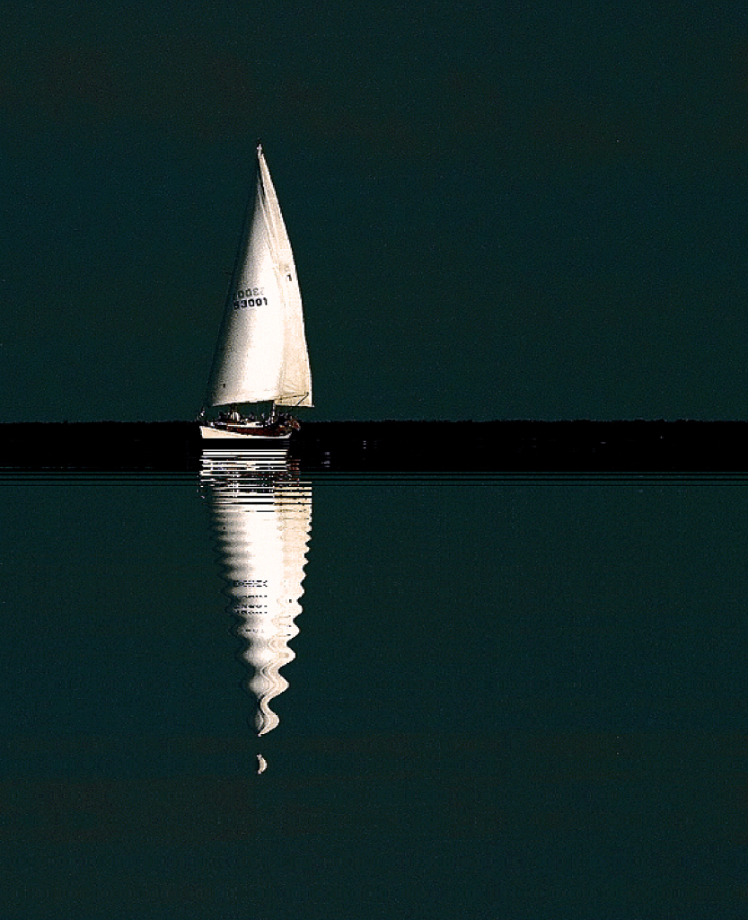 Sailboat surrounded by dark sky and reflecting on calm dark water