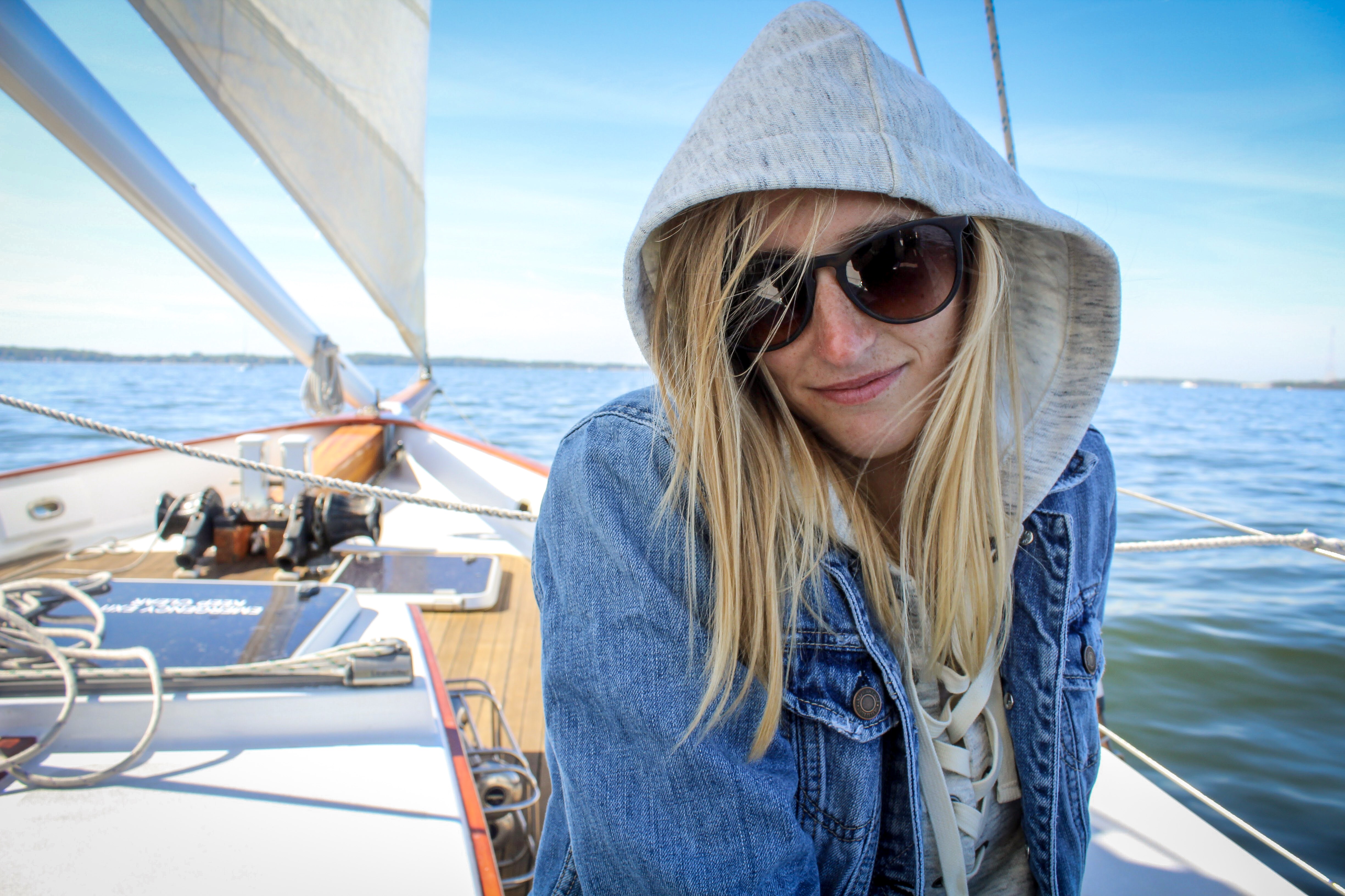 Pretty young women in hoodie and sunglasses sailing on a sunny day