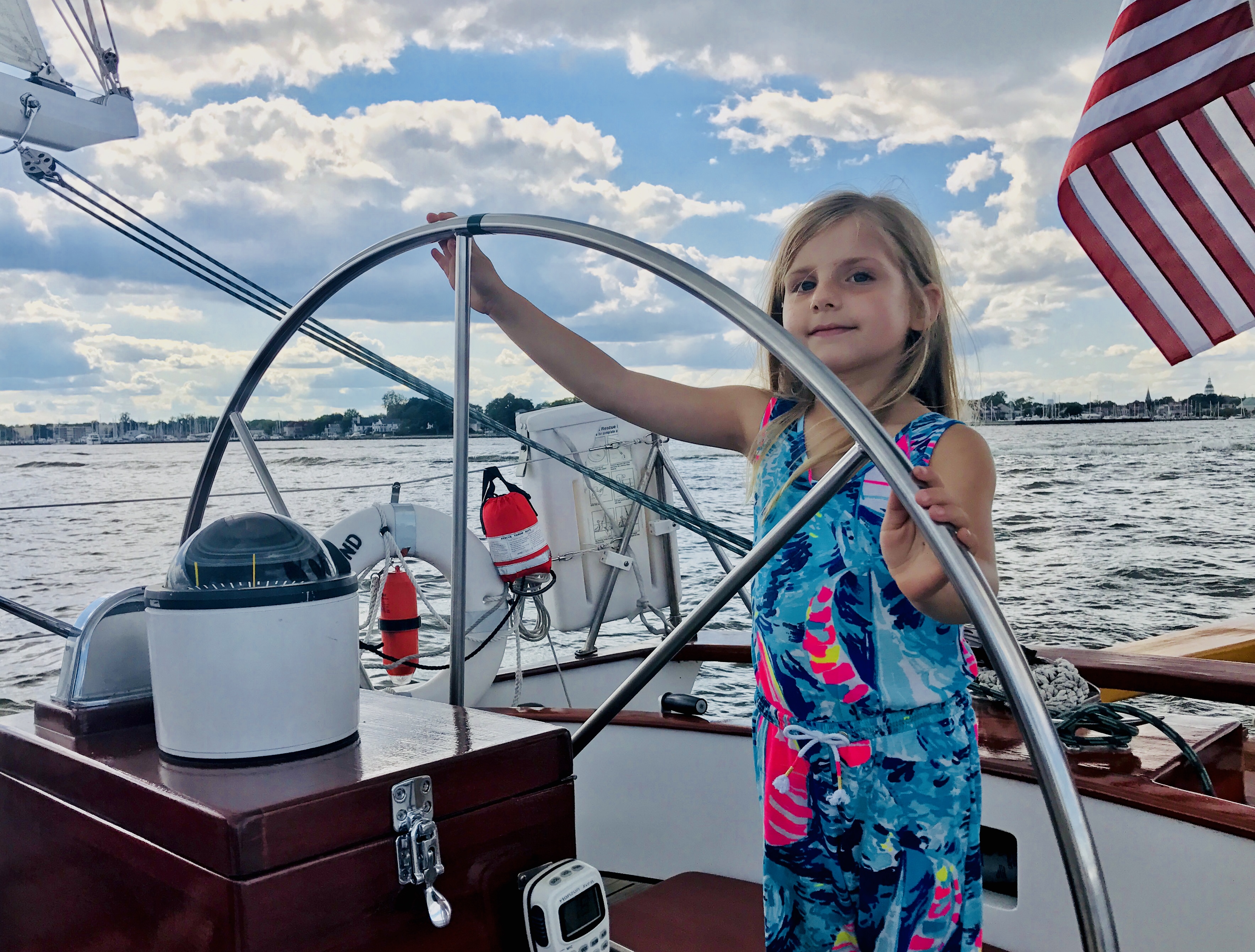Small girl with sailboat sundress captaining the helm with a smile