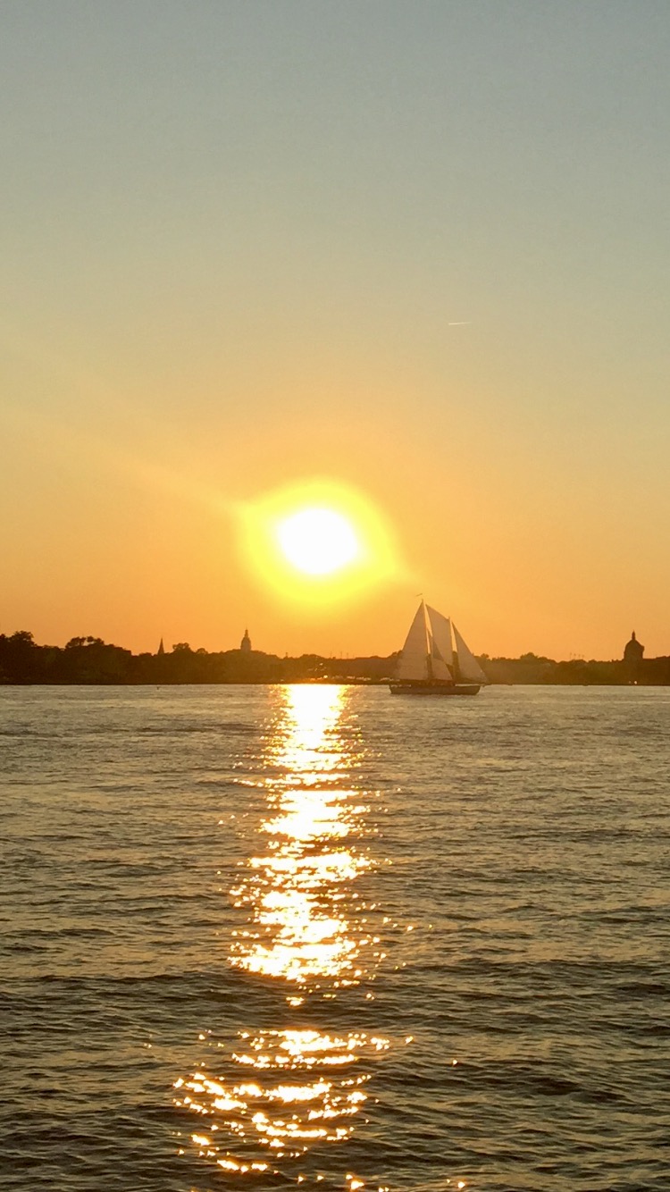 Giant yellow sun shining on schooner in blue waters