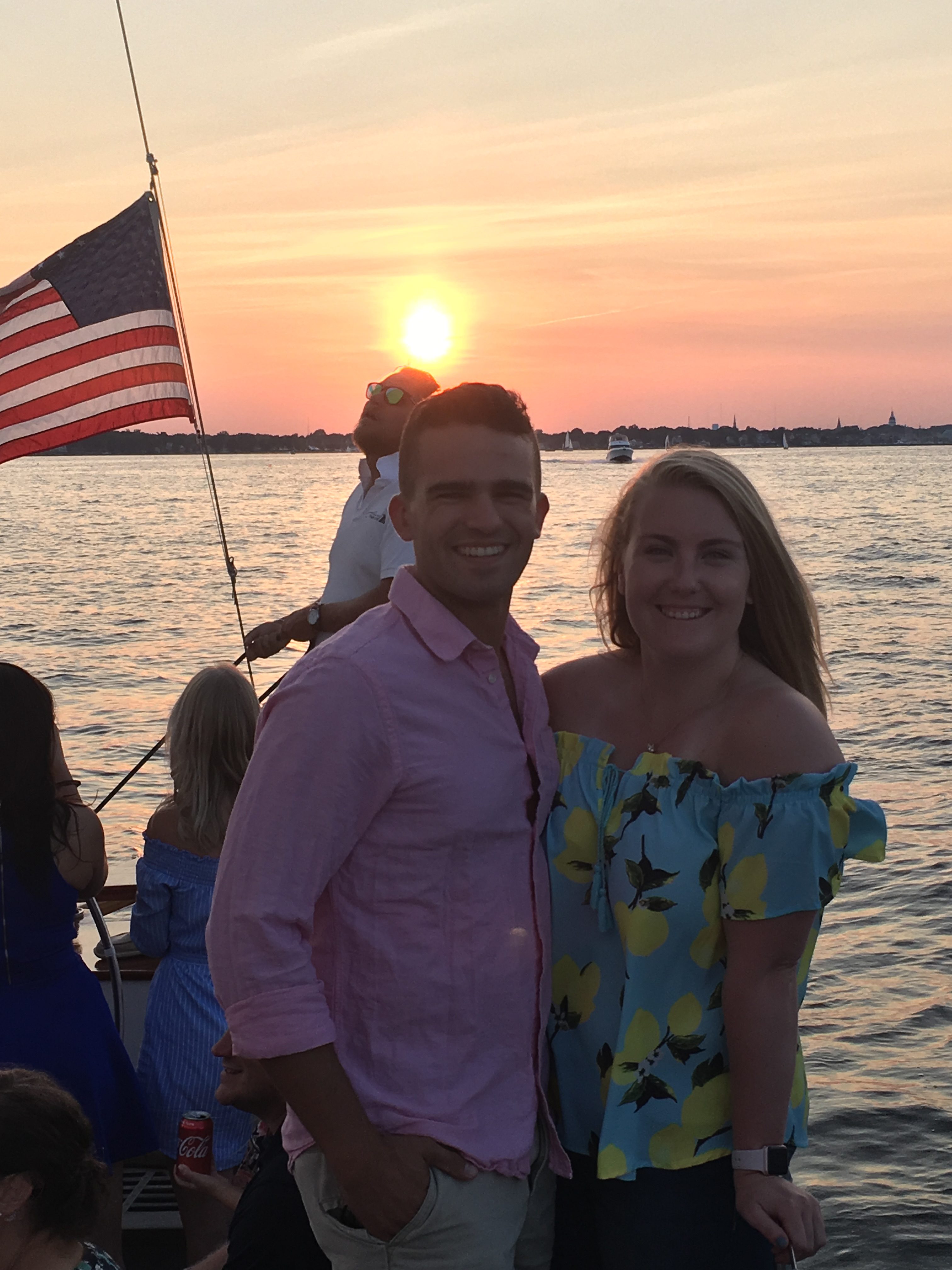 Smiling young couple on boat with American Flag and bright sunset