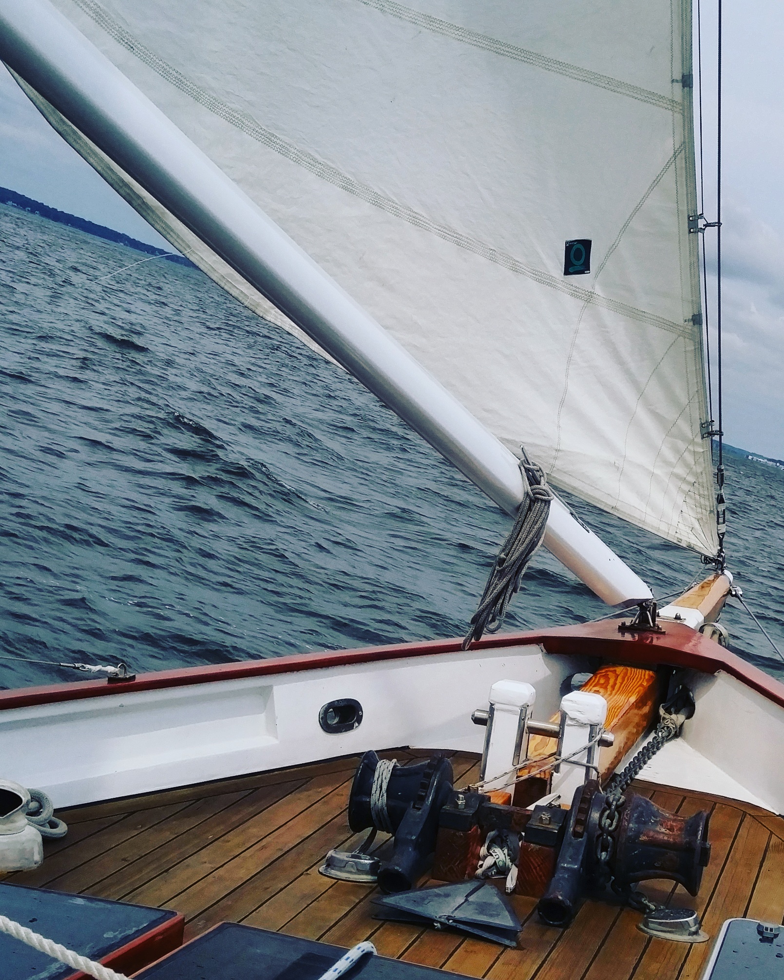 Bow of schooner with section of sail and boom and blue water ahead