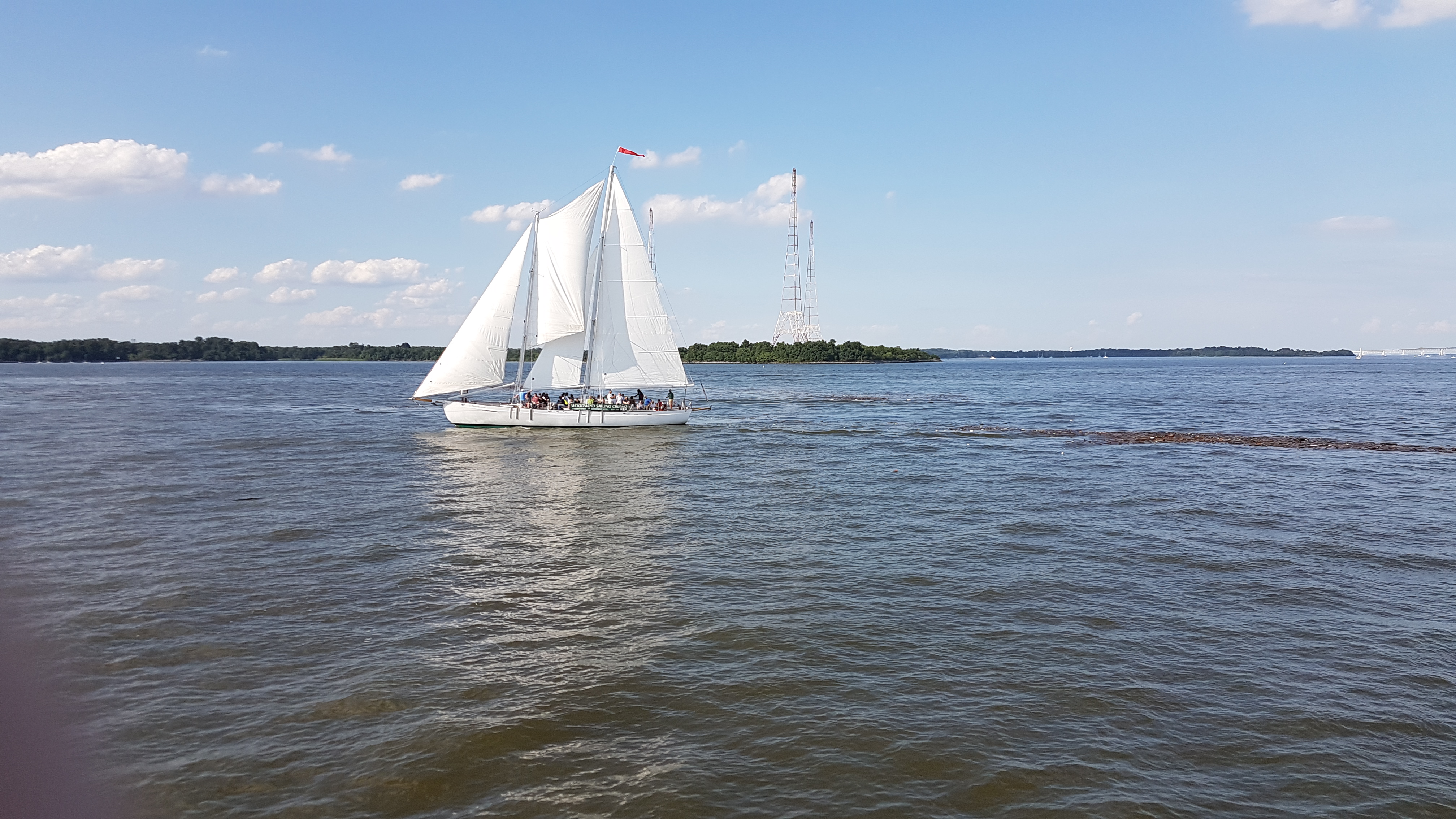 Schooner sailing with radio towers in back ground on calm waters