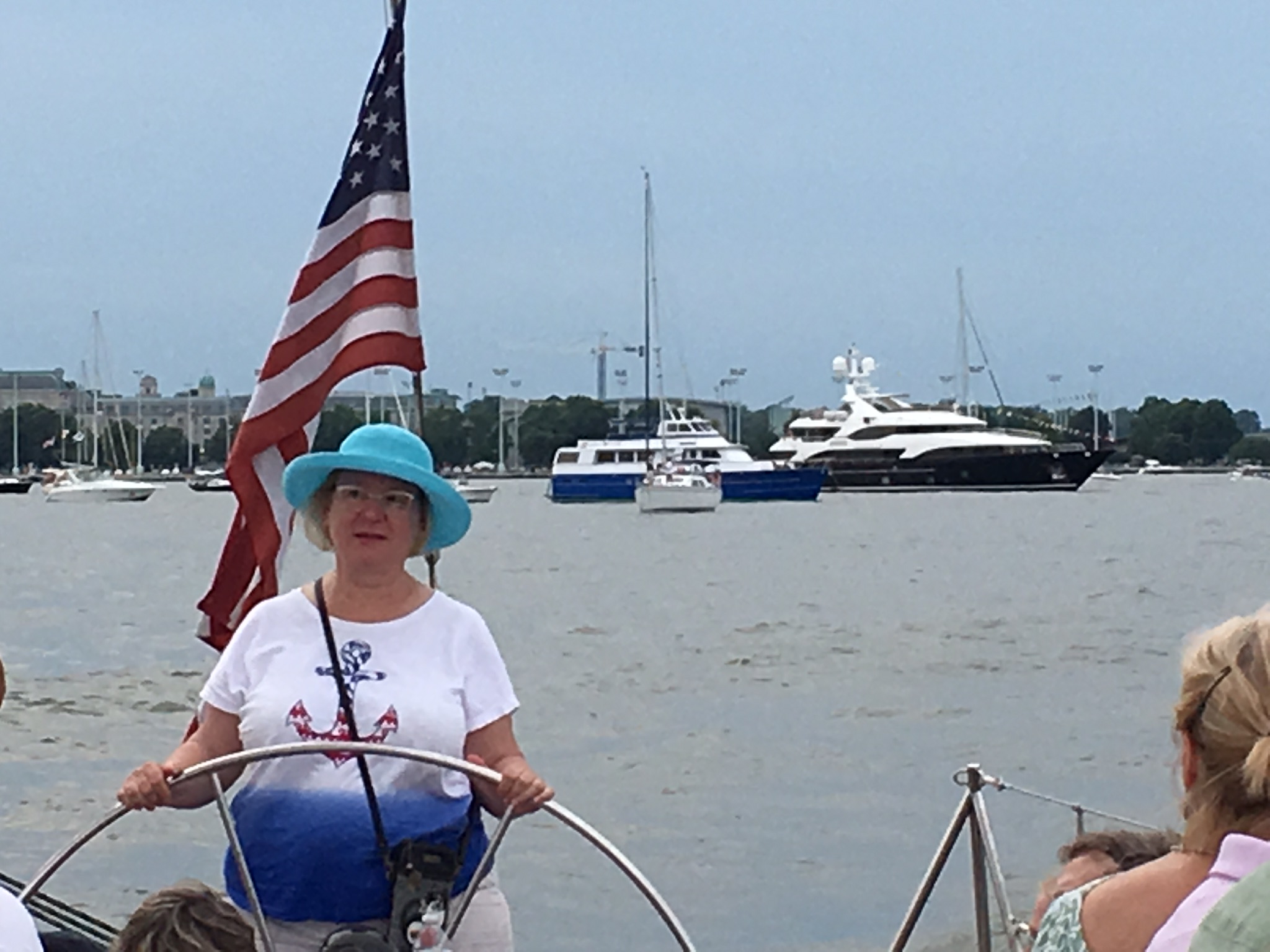 Women in blue hat steering the boat with Yachts in the background