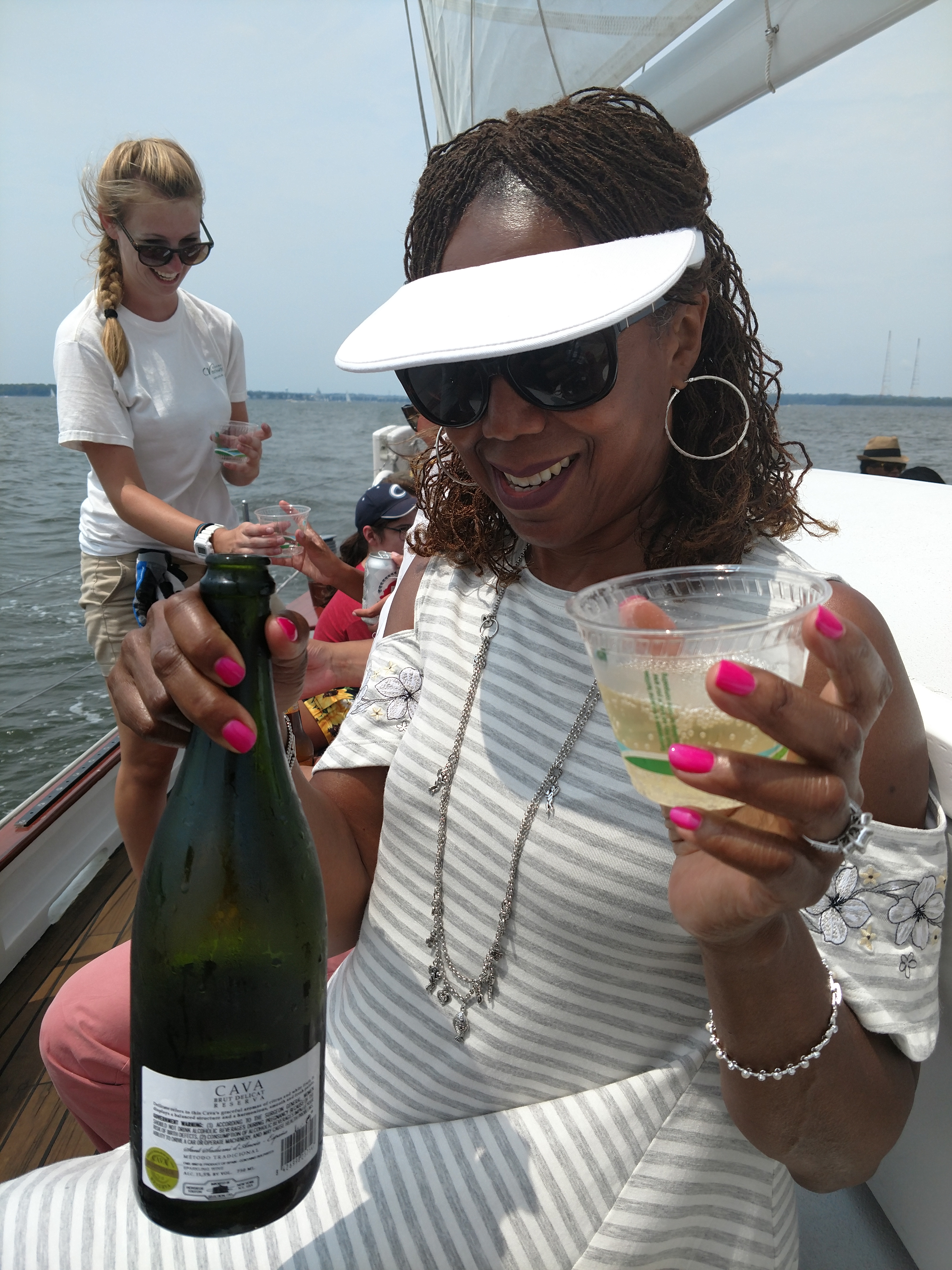 Women holding up bottle of bubbly and glass on a sail