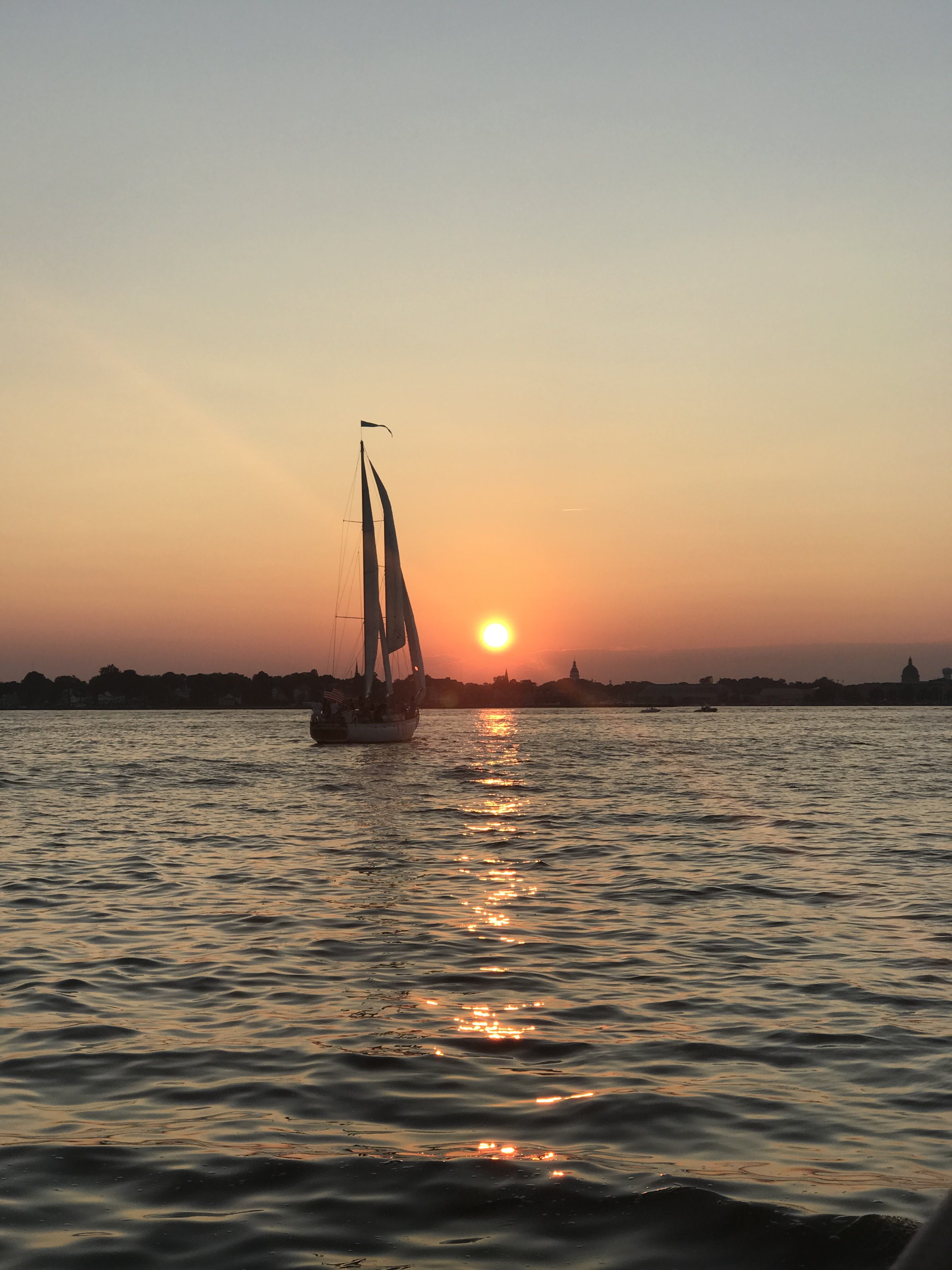 Schooner on the water with a big orange sun over blue waters