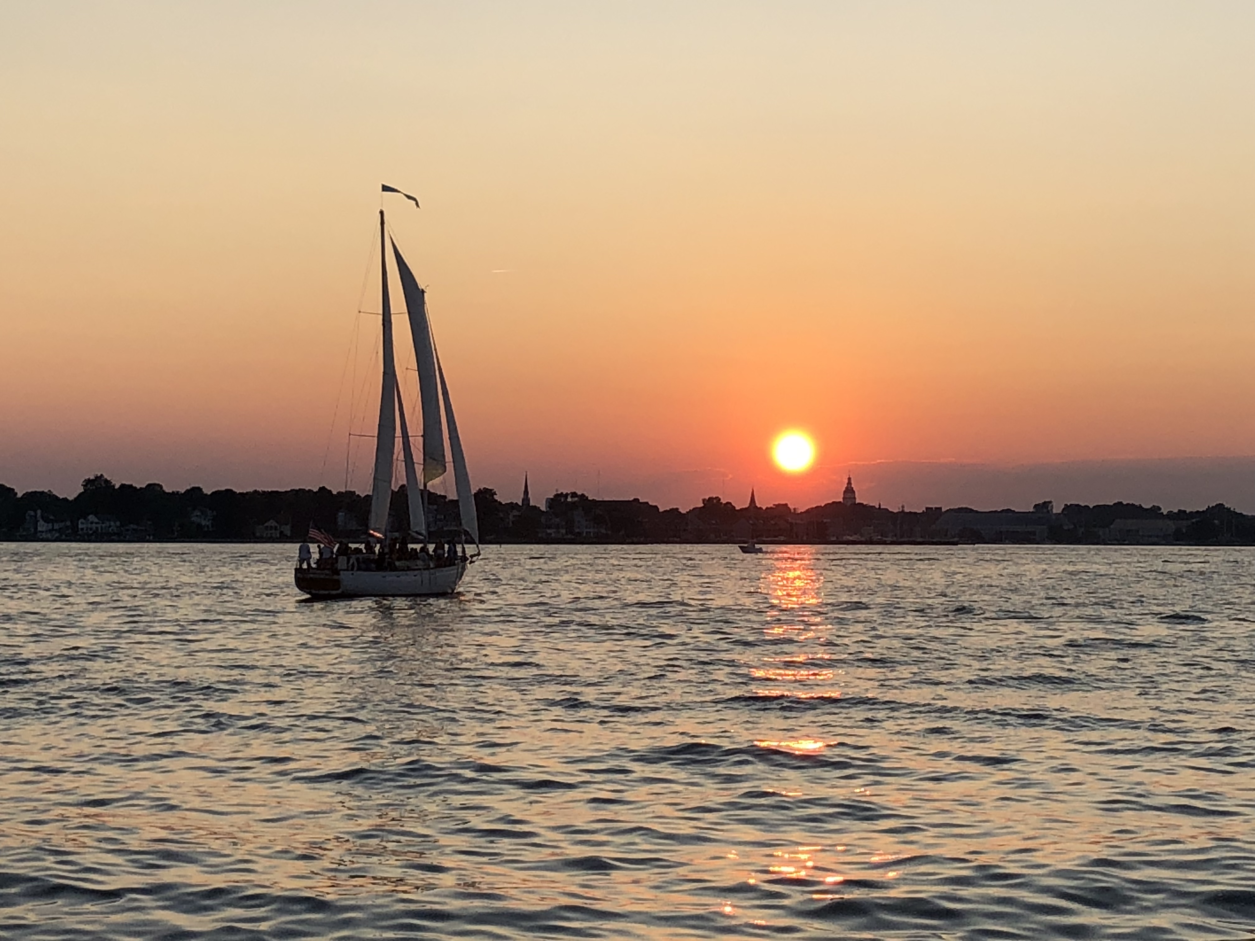 Schooner on the water with a big orange sun over blue waters