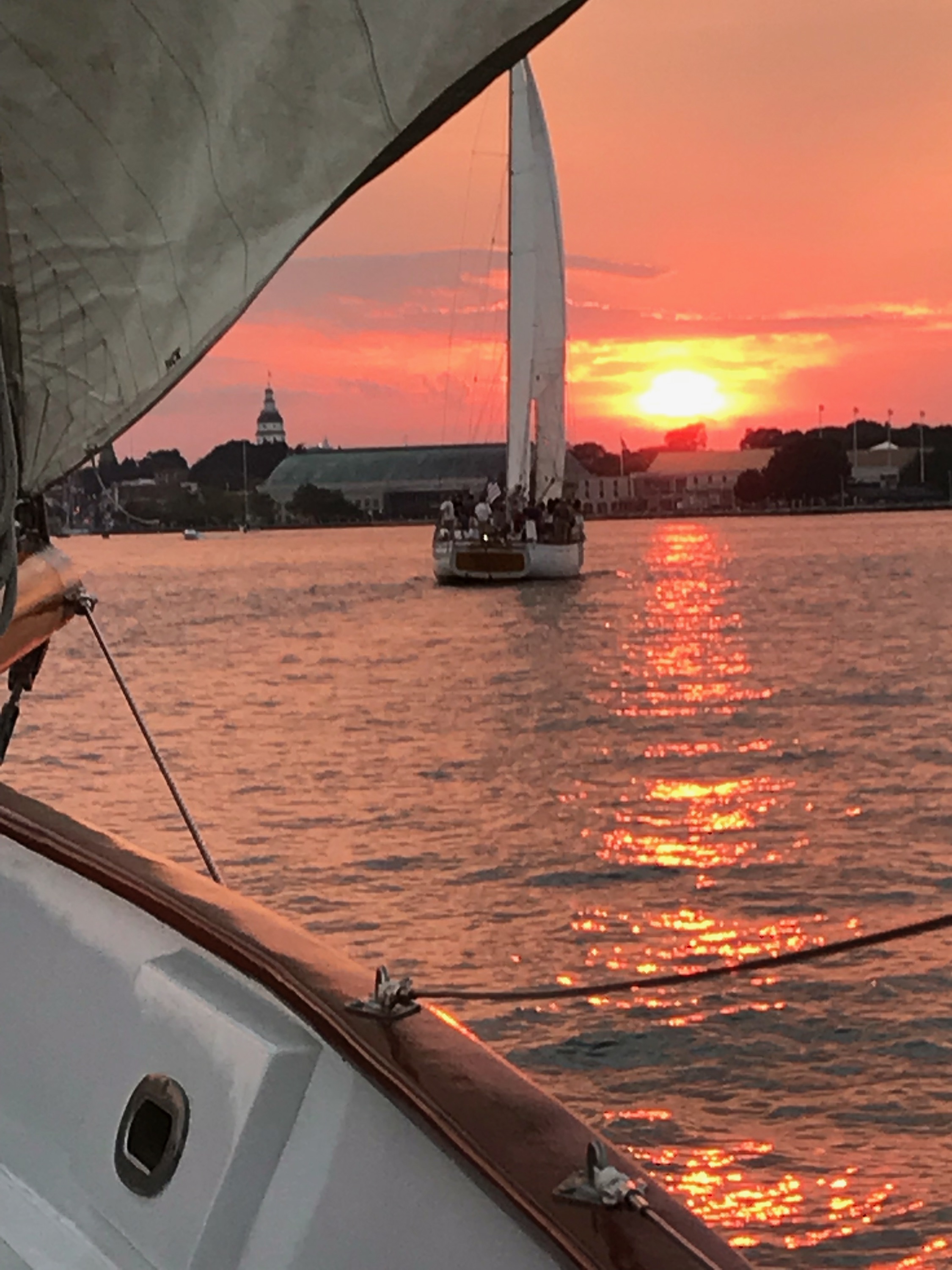 Schooners following each other into a bright orange and red sunset