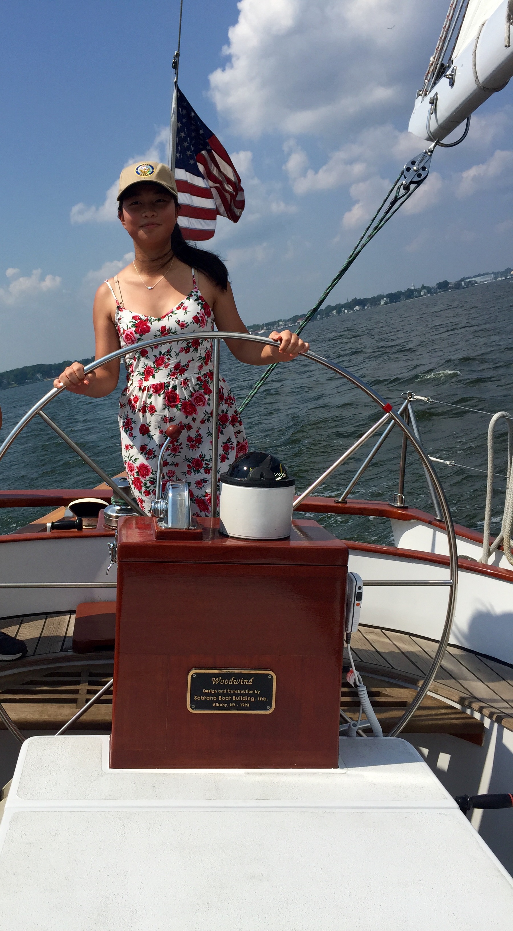 Young girl in a sundress steering the boat with blue skies