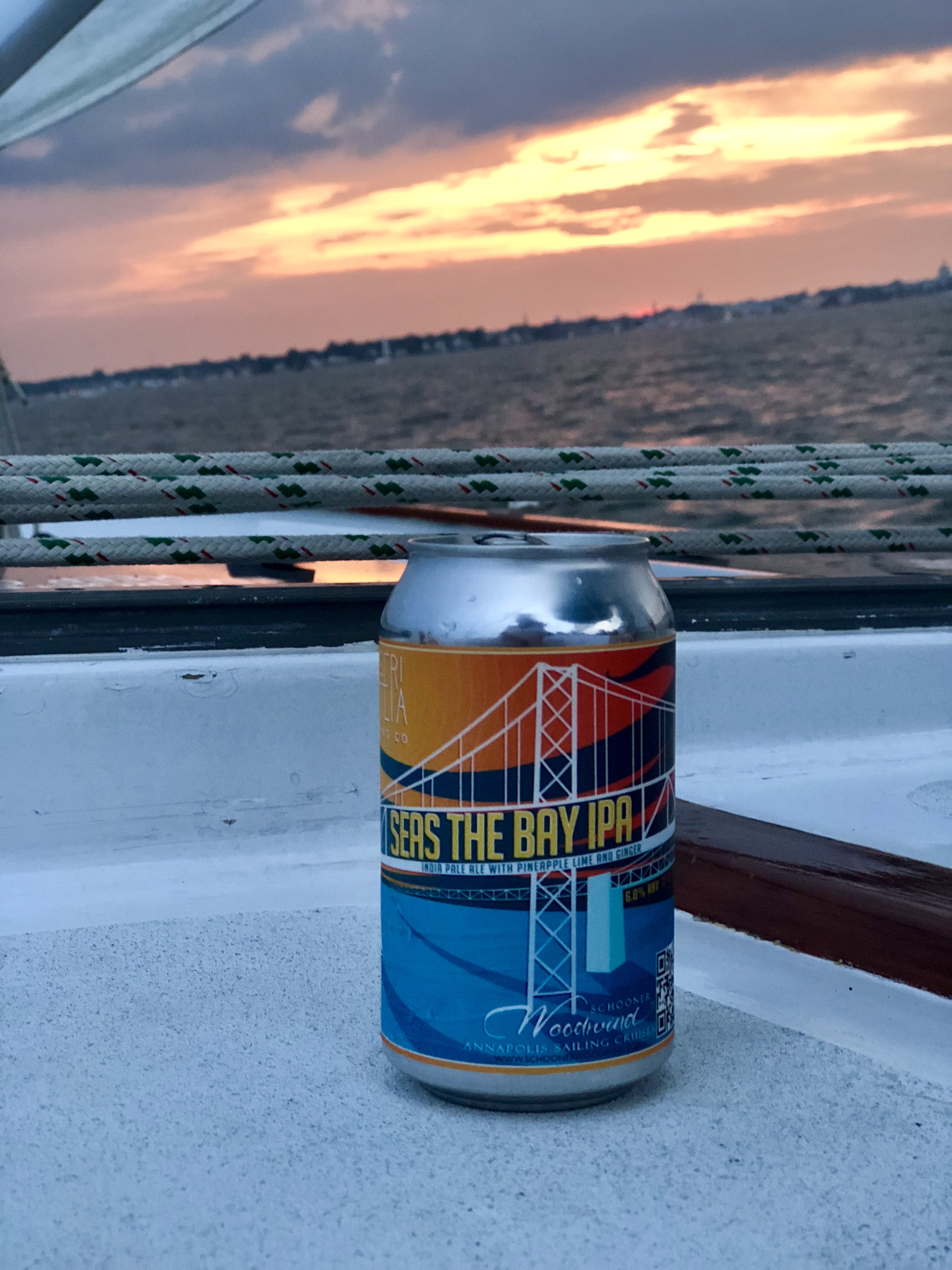 Seas the Bay IPA sitting on the deck with pretty sunset behind it