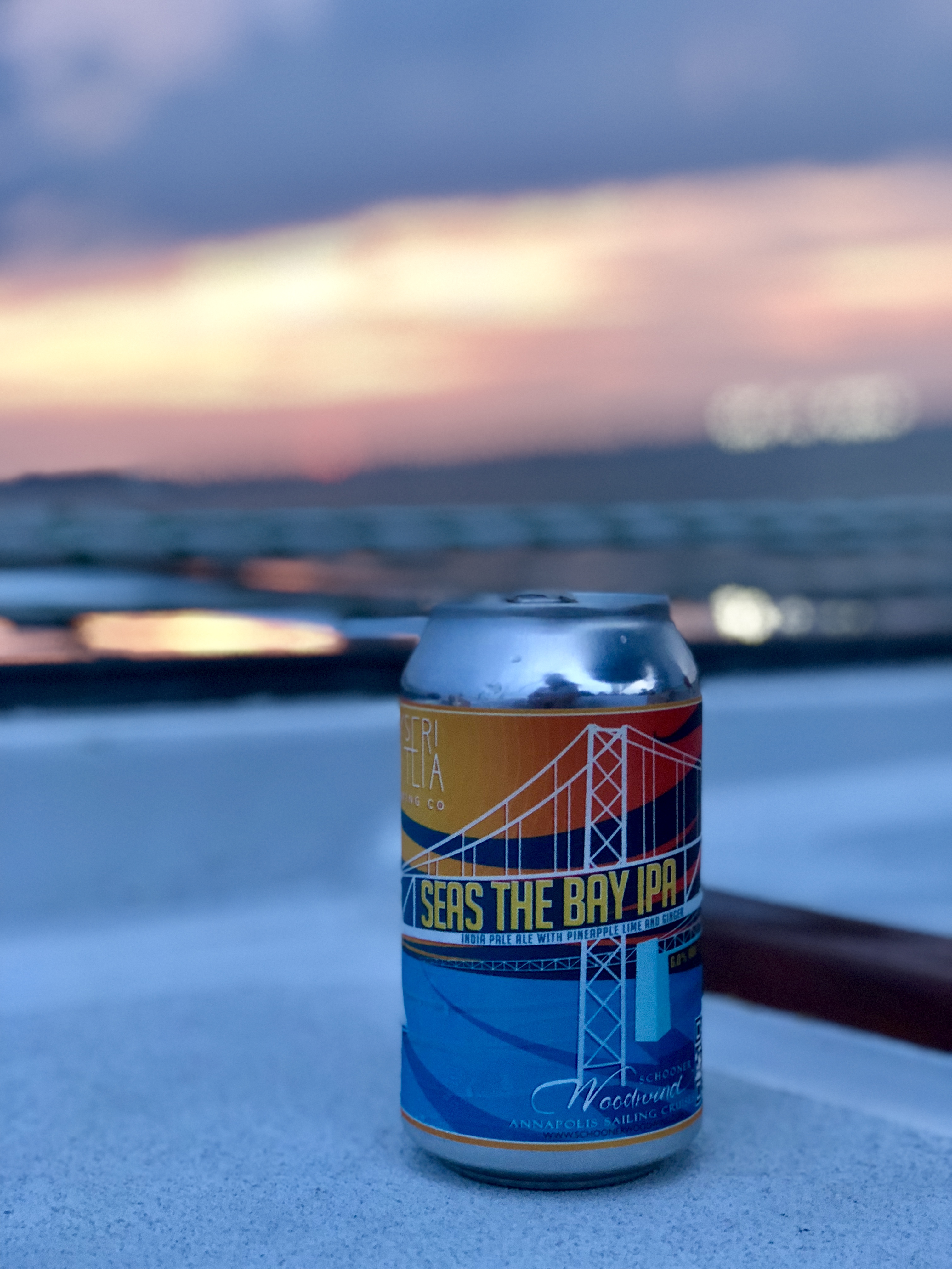 Seas the Bay IPA sitting on the deck with pretty sunset behind it