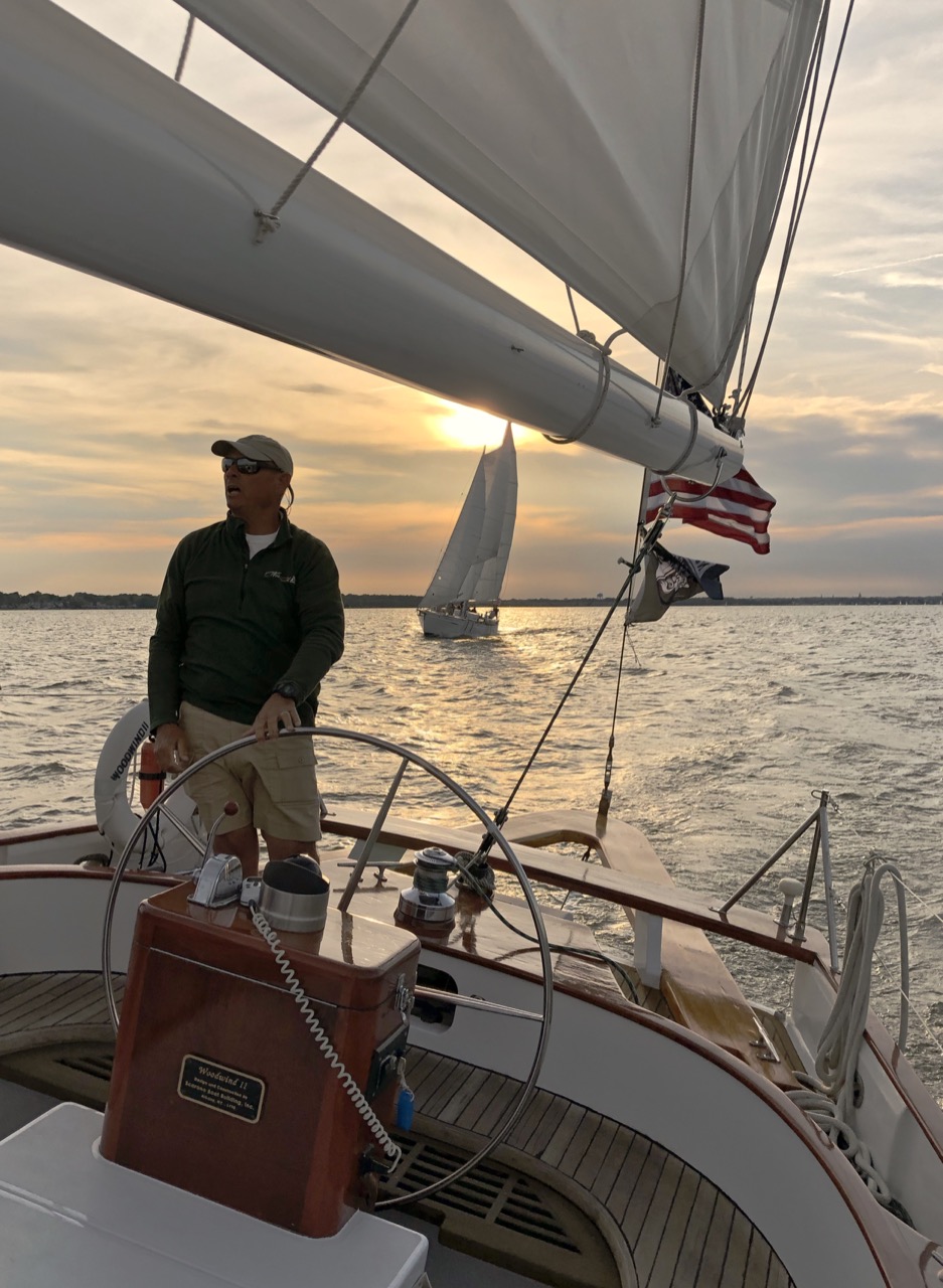 Captain steering helm with second schooner following at sunset