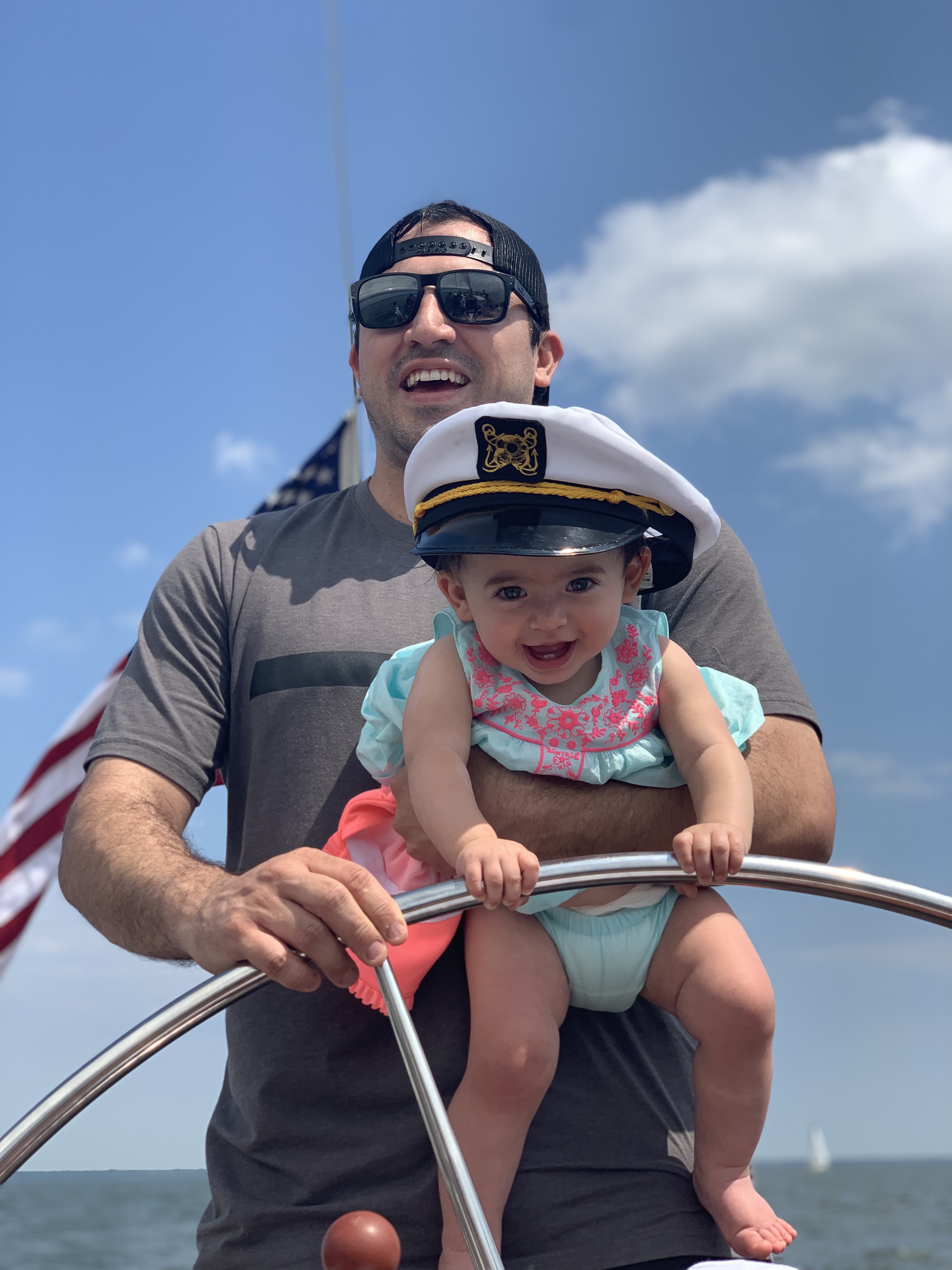 Man holding smiling baby in captain's hat who is helping him steer