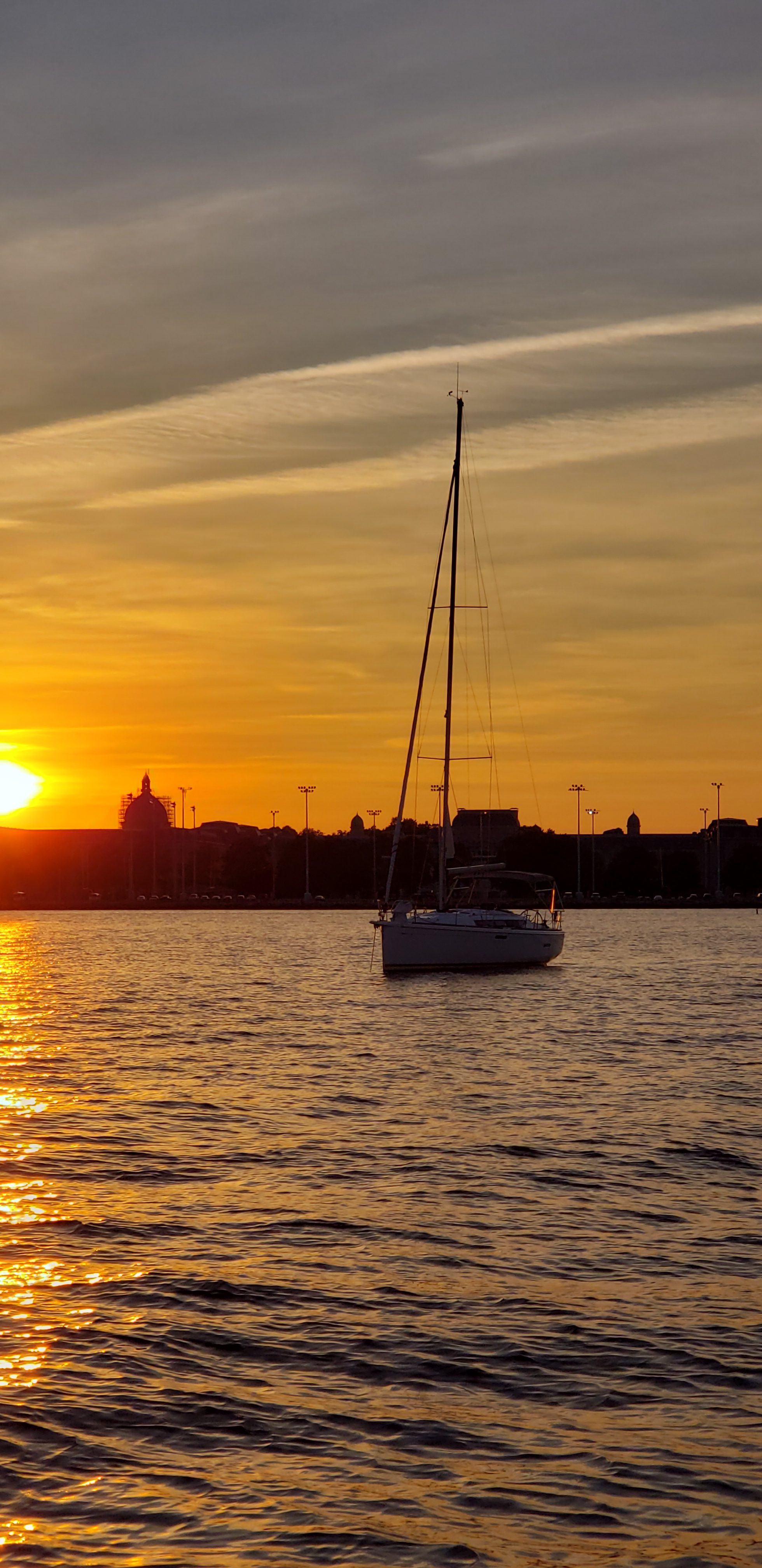 Sail boat with sails down and sunset behind it on the water