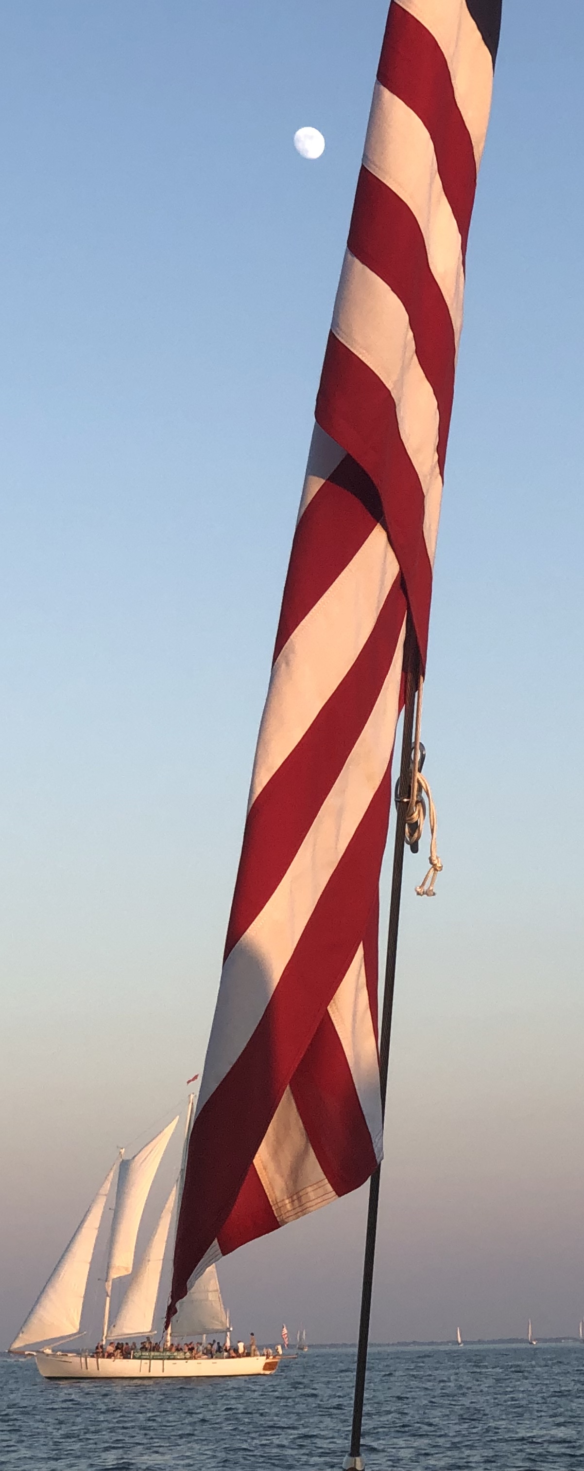Schooner sailing behind American flag with Moon shining high in sky