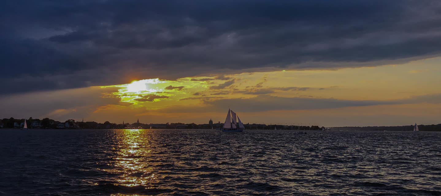 Dark clouds with a bright yellow sunset showing and dark waters with schooner sailing on them
